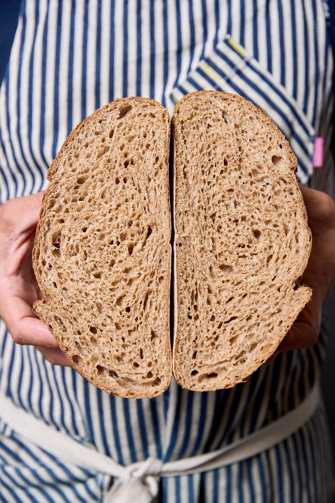 Person holding two halves of a sliced loaf of bread with a striped shirt in the background.