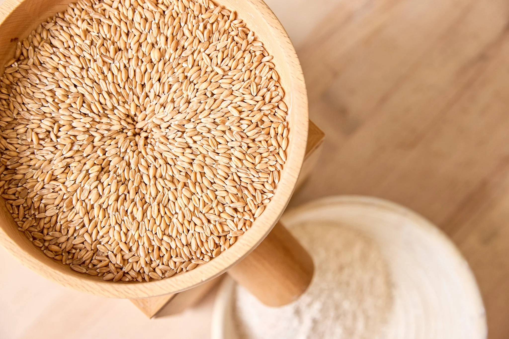 Top-down view of a wooden container filled with wheat grains, with a container of flour partially visible below.