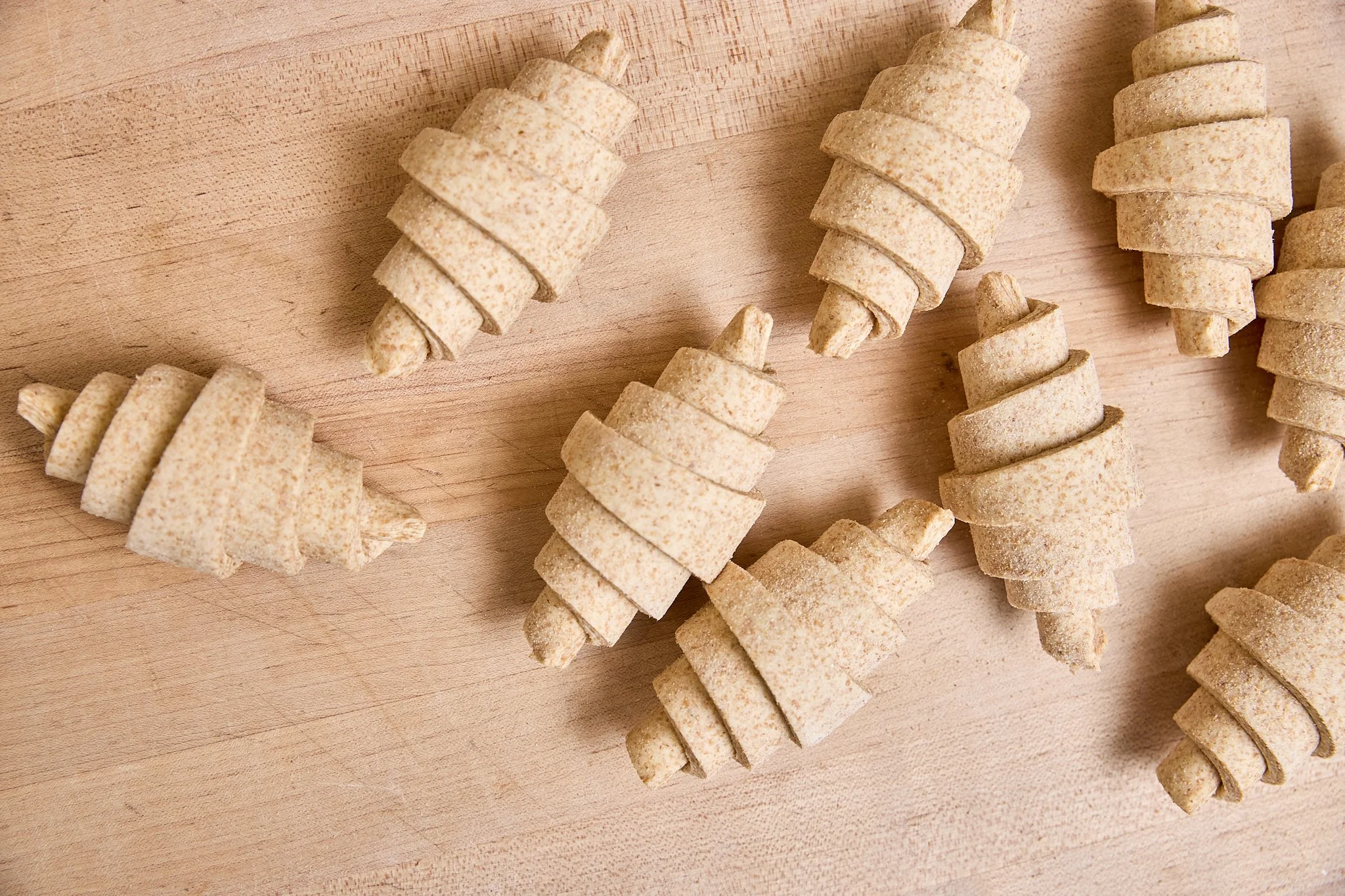Several uncooked croissants on a wooden surface.