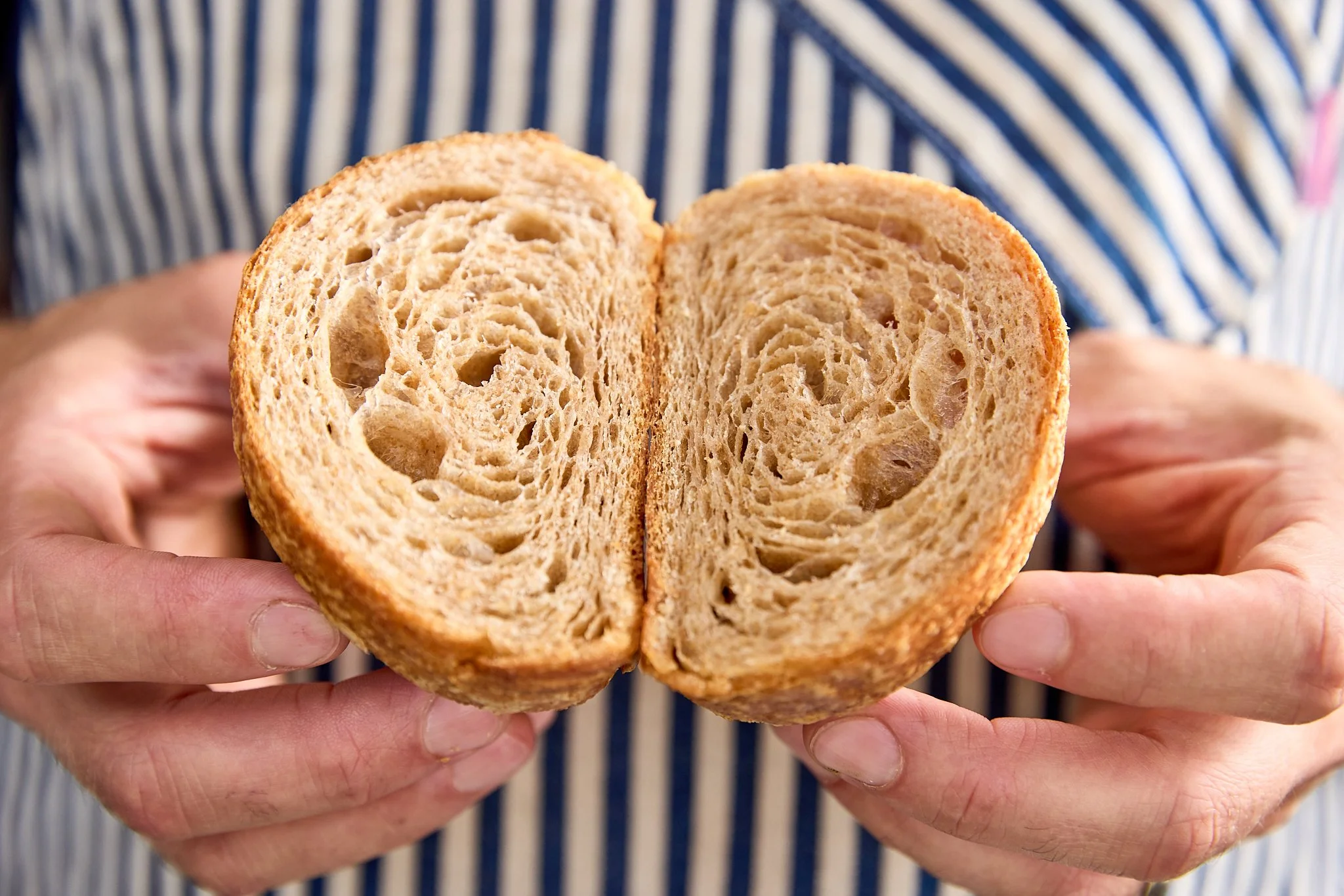 A person holding a halved loaf of bread with a golden-brown crust and soft, airy interior.