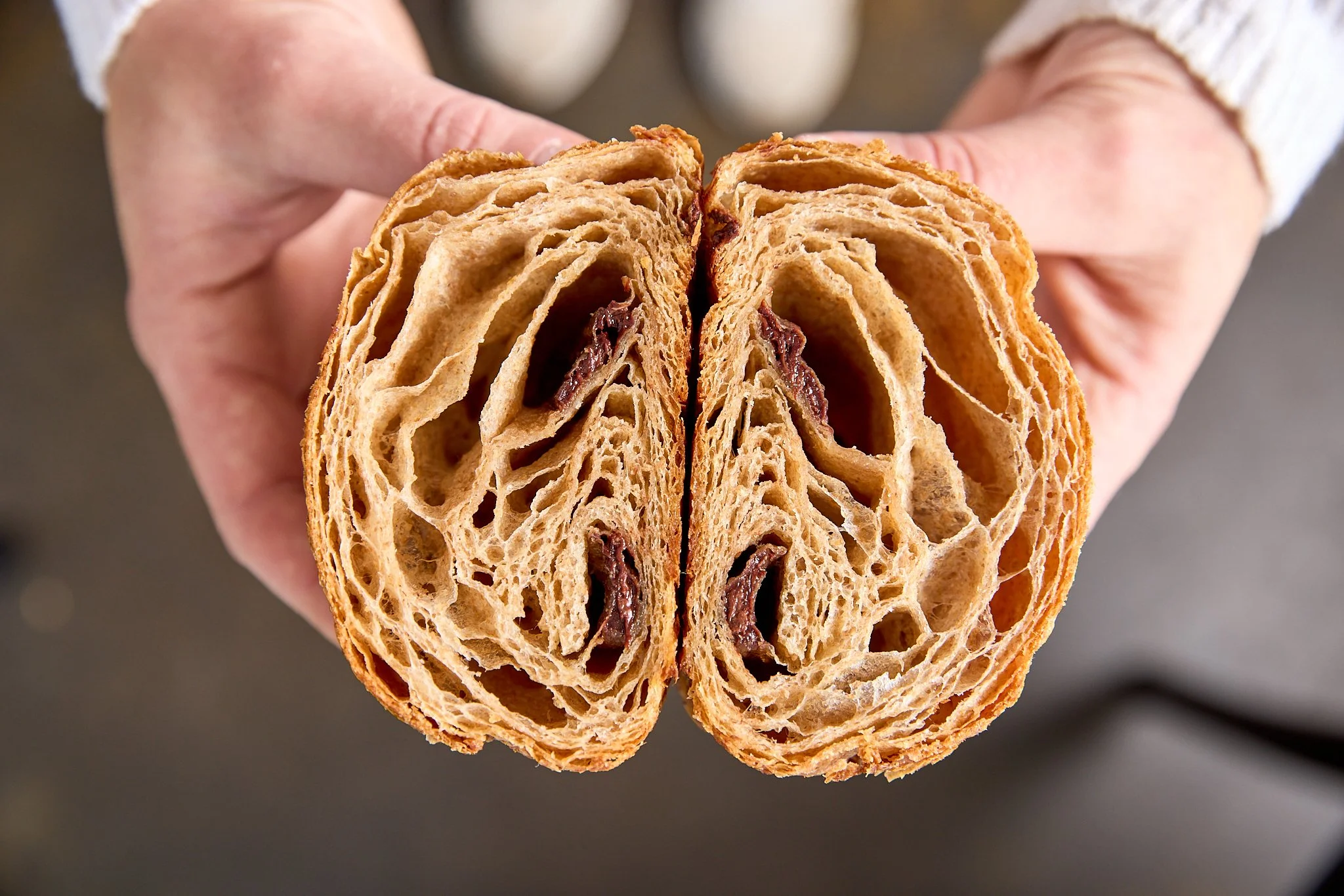 A person holding a cross-section of a flaky, golden-brown pastry with a dark filling inside.