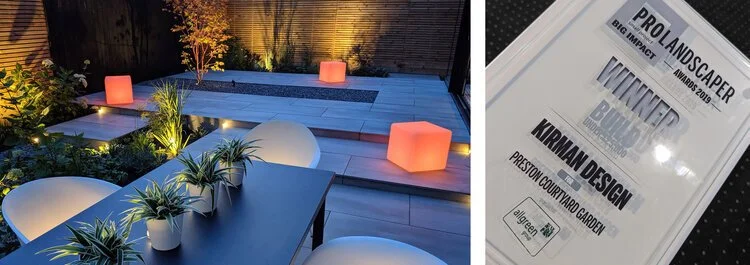 Nighttime outdoor patio with modern furniture, illuminated planters, and decorative lighting, alongside a framed award certificate for landscape design.