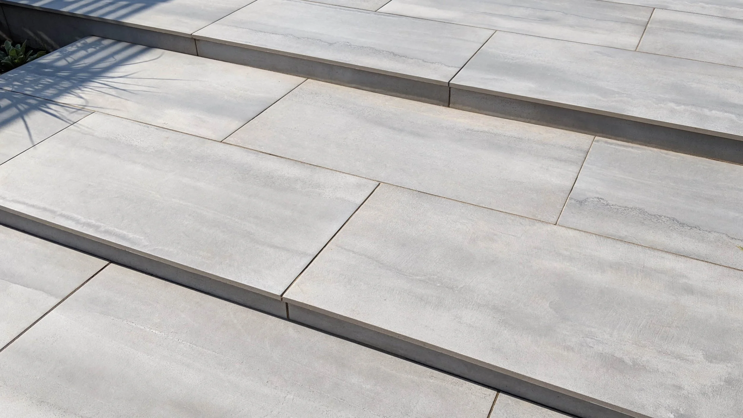 Close-up view of light-colored stone or concrete steps with shadows cast on the surface.
