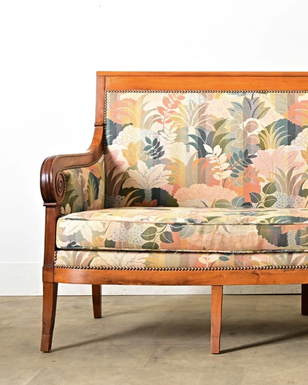 French 19th Century Restauration Fruitwood Settee with scrolled arms coiled to volutes enclose the tall, tightly upholstered seat back above a single bench cushion upholstered in a fantastic jacquard of botanical theme in a muted, pastel color palett
