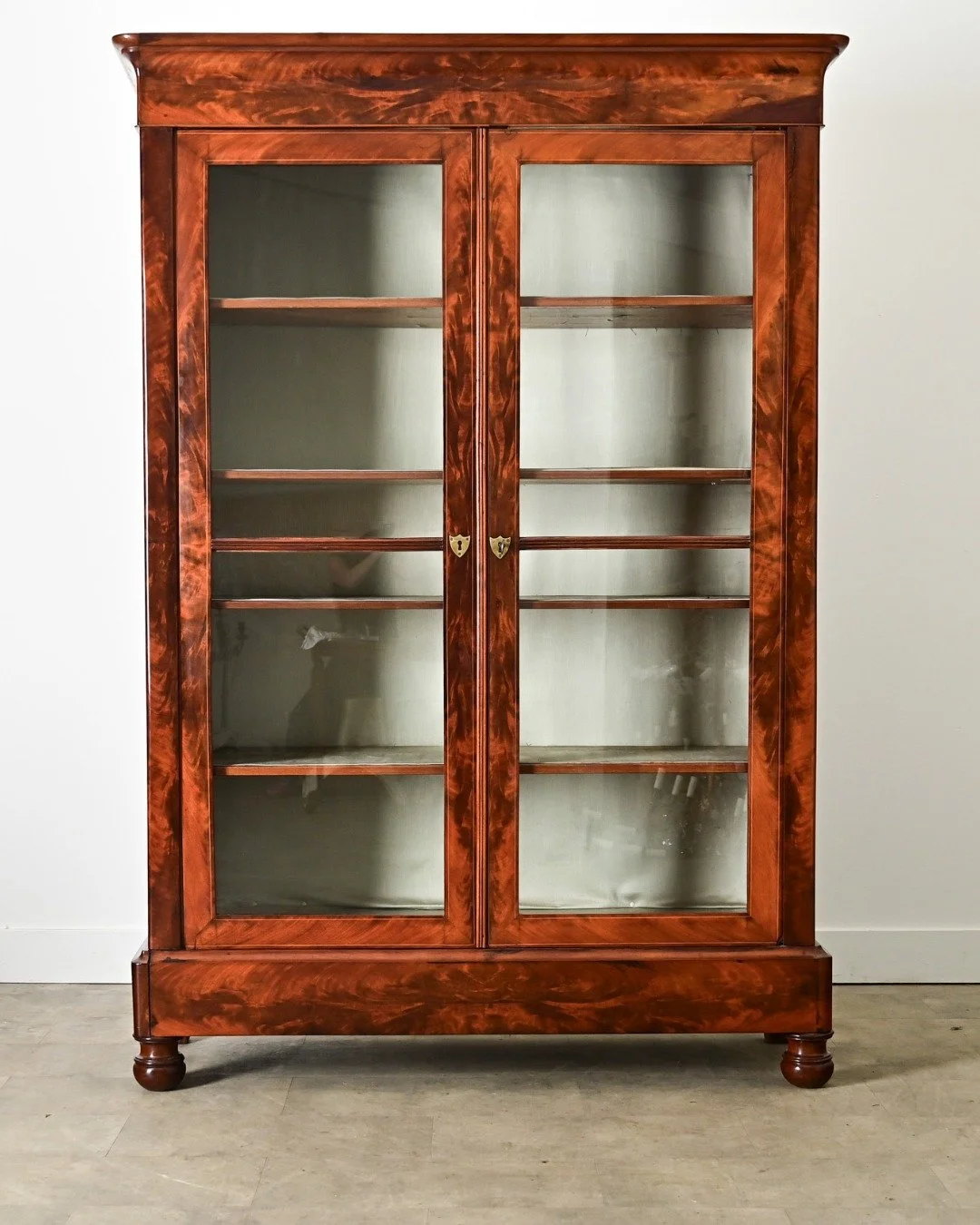 French 19th Century Mahogany Bibliotheque or display cabinet, handcrafted in Louis Philippe style from gorgeously figured mahogany. Behind the locking doors with their original, wavy glass panes are four interior shelves, adjustable on sawtooth brack