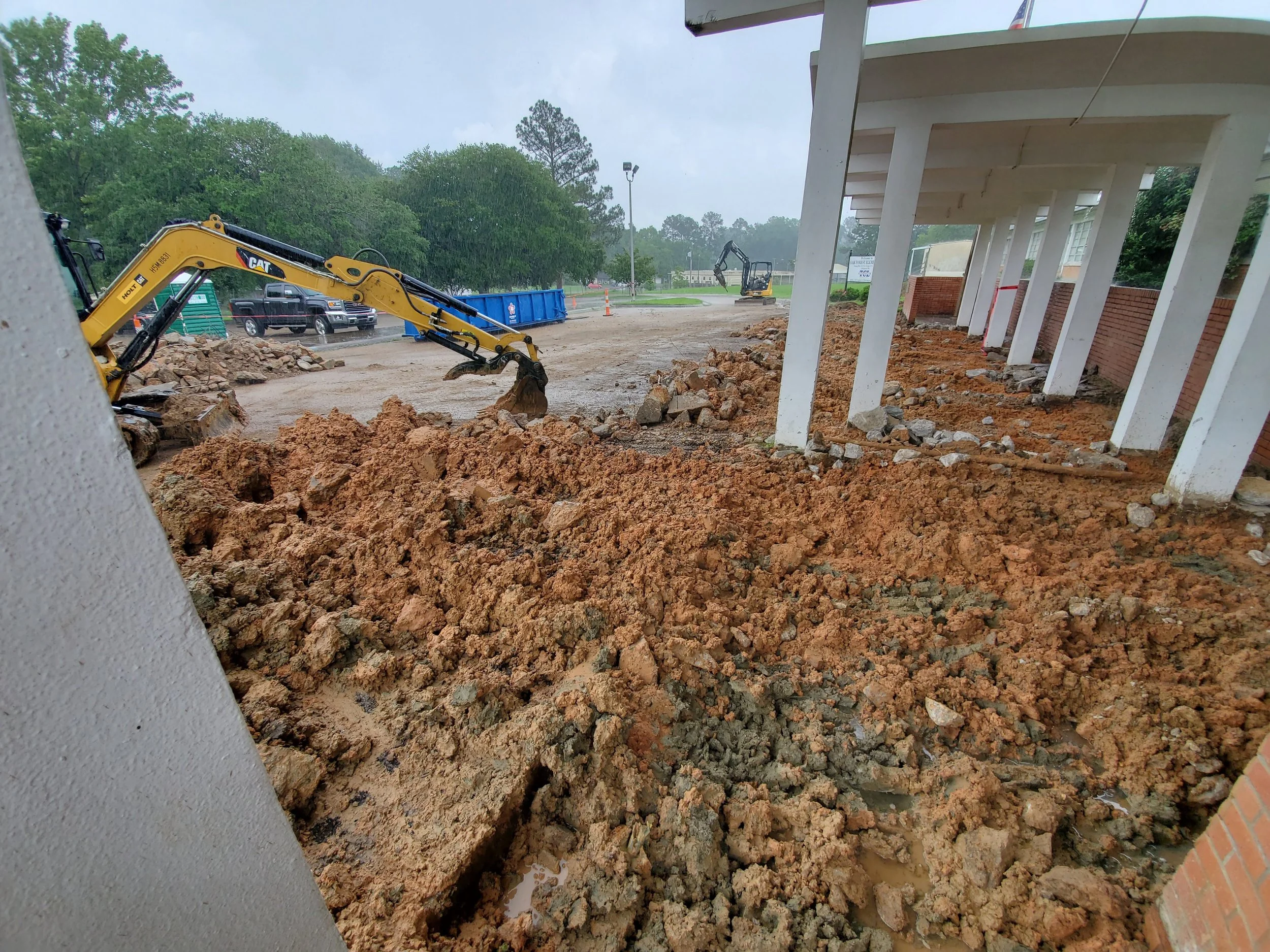 Construction site with muddy ground, excavators, and building columns.