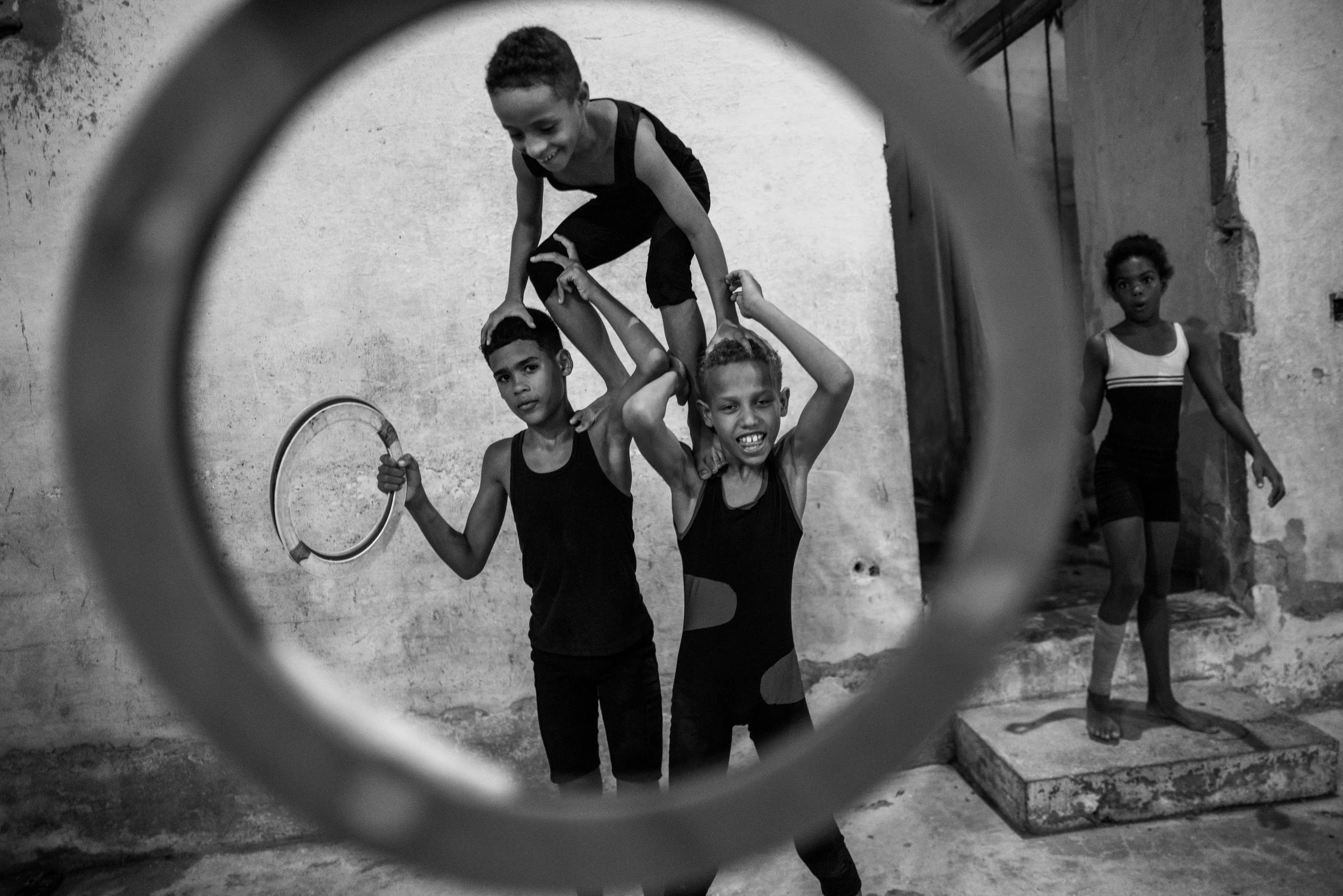Group of children playing and balancing with rings in a rustic indoor space, seen through a circular frame.