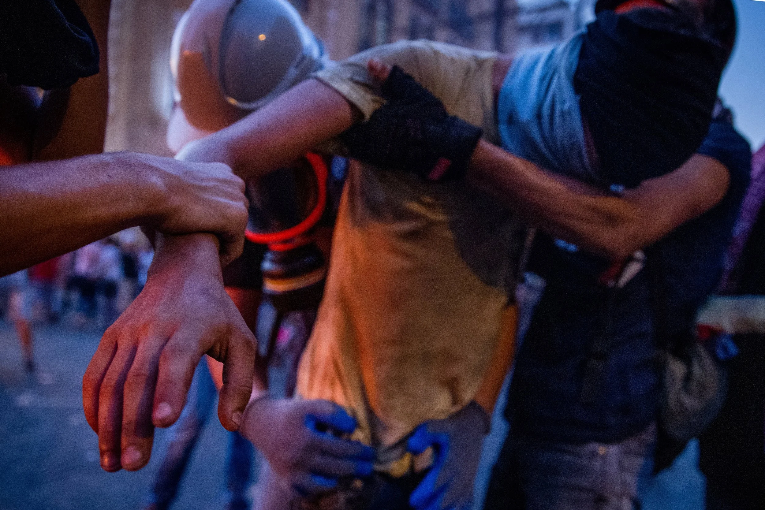 A rescue worker is holding a person's arm during a rescue operation at dusk or nighttime. The person being assisted is wearing a helmet and appears to be in distress.