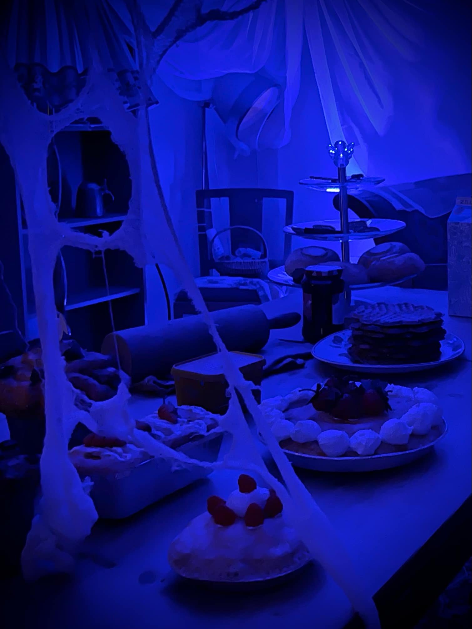 Table with desserts and Halloween decorations in blue lighting.