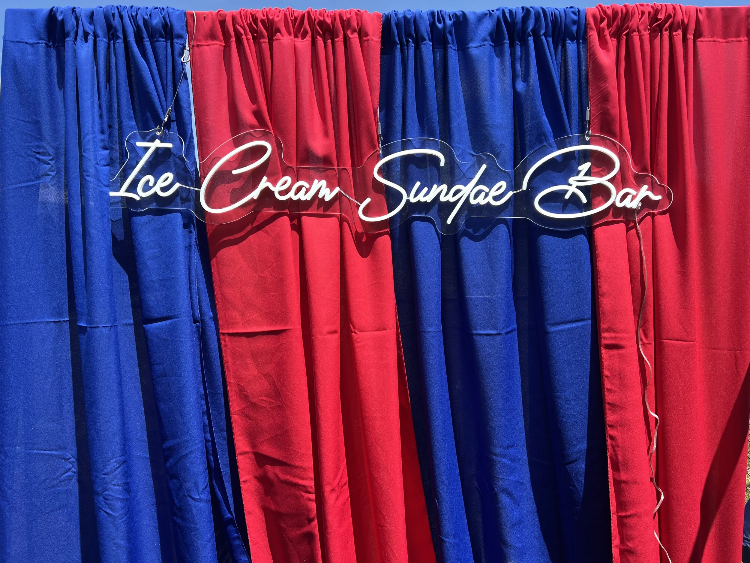 Blue and red cloth curtains with a neon sign that reads 'Ice Cream Sundae Bar' hanging in front of them.