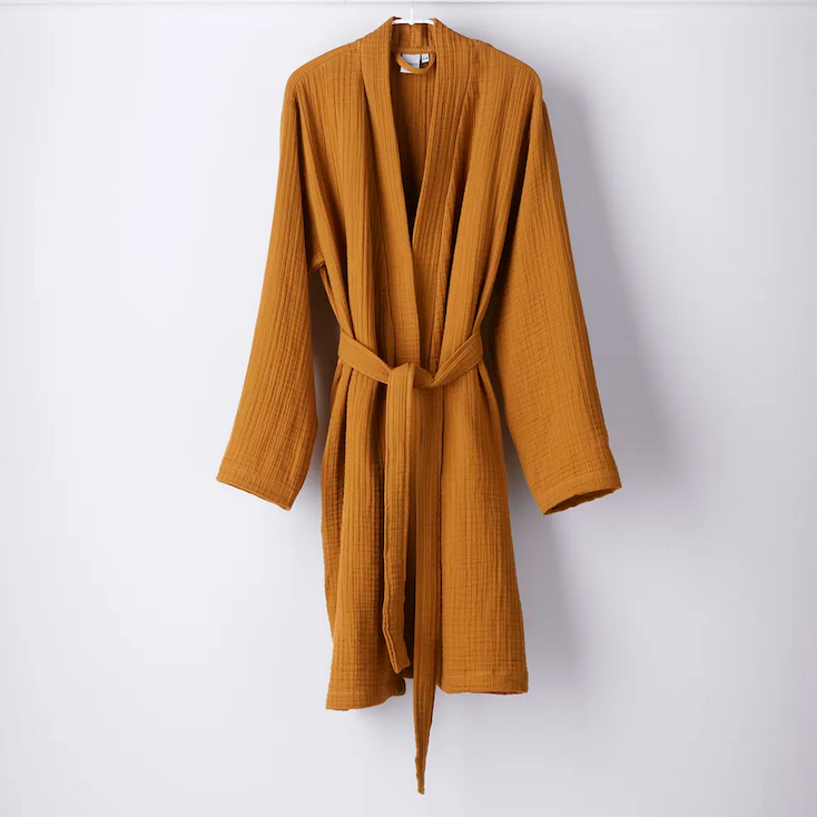 Mustard-colored robe with a textured, lightweight fabric hanging against a white wall