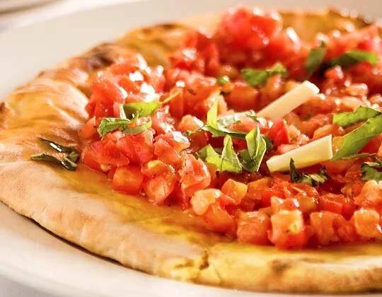 Close-up of a pizza with tomato chunks, chopped green herbs, and cheese on a thin crust.