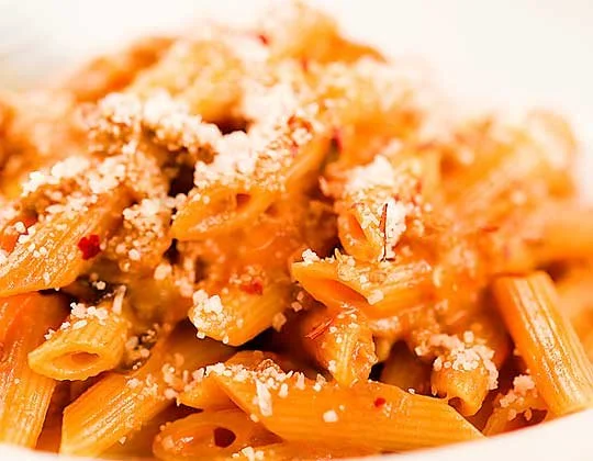 Close-up of cooked penne pasta with tomato sauce and grated cheese