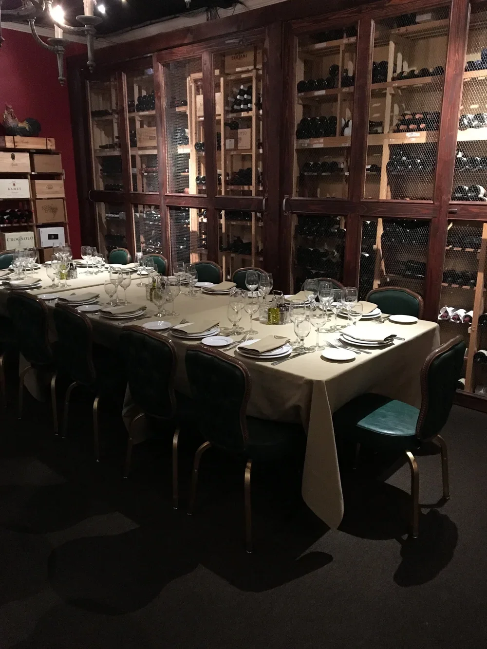 A banquet table set for a formal dinner with white napkins, wine glasses, and silverware in a wine cellar, with wooden wine racks filled with wine bottles in the background.
