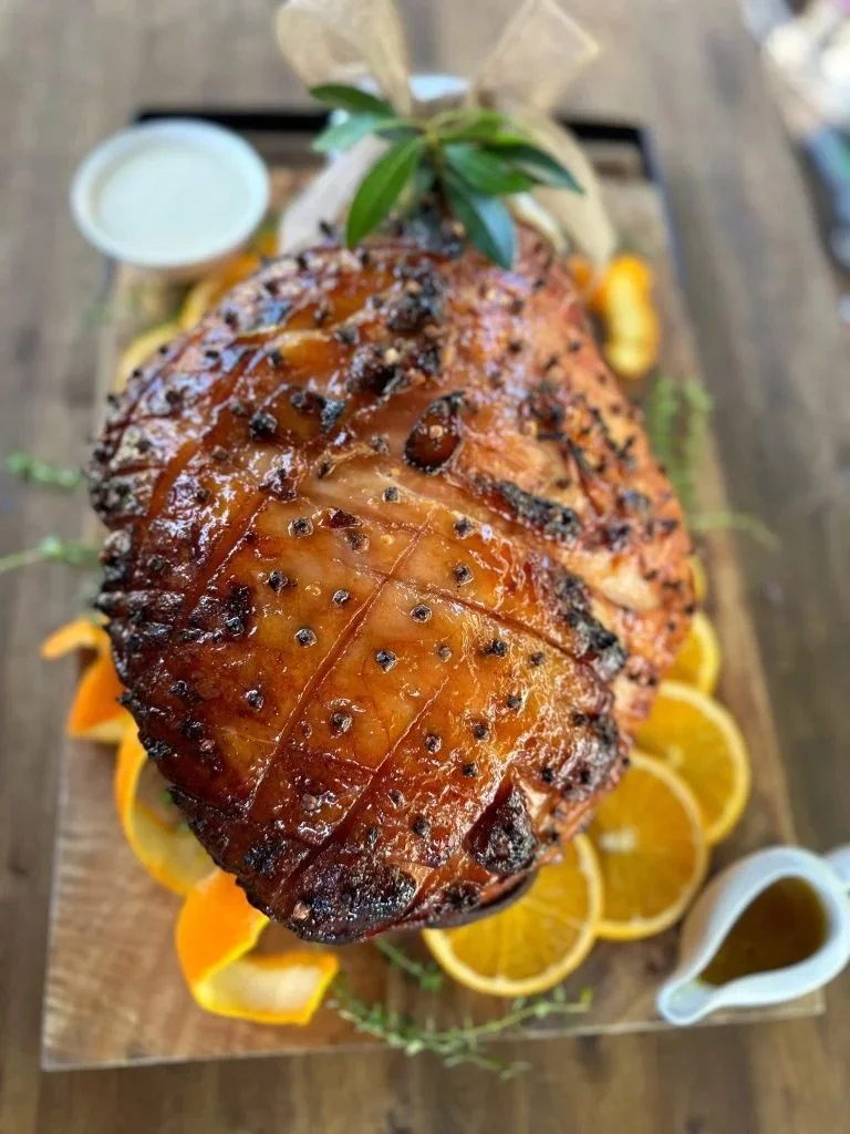 oast Christmas Ham with cloves, oranges sitting on orange slices, bread board and bay leaves. Daylesford Meat Co Christmas Ham made from free-range Otway Pork