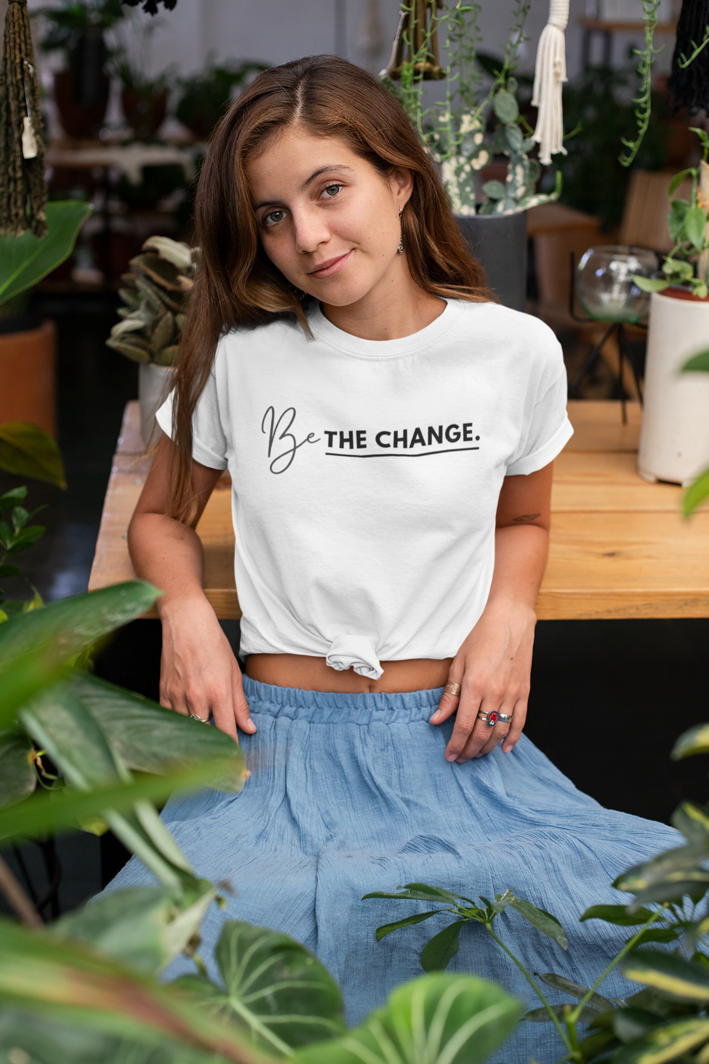 knotted-t-shirt-mockup-of-a-woman-at-a-table-surrounded-by-plants-27083.png