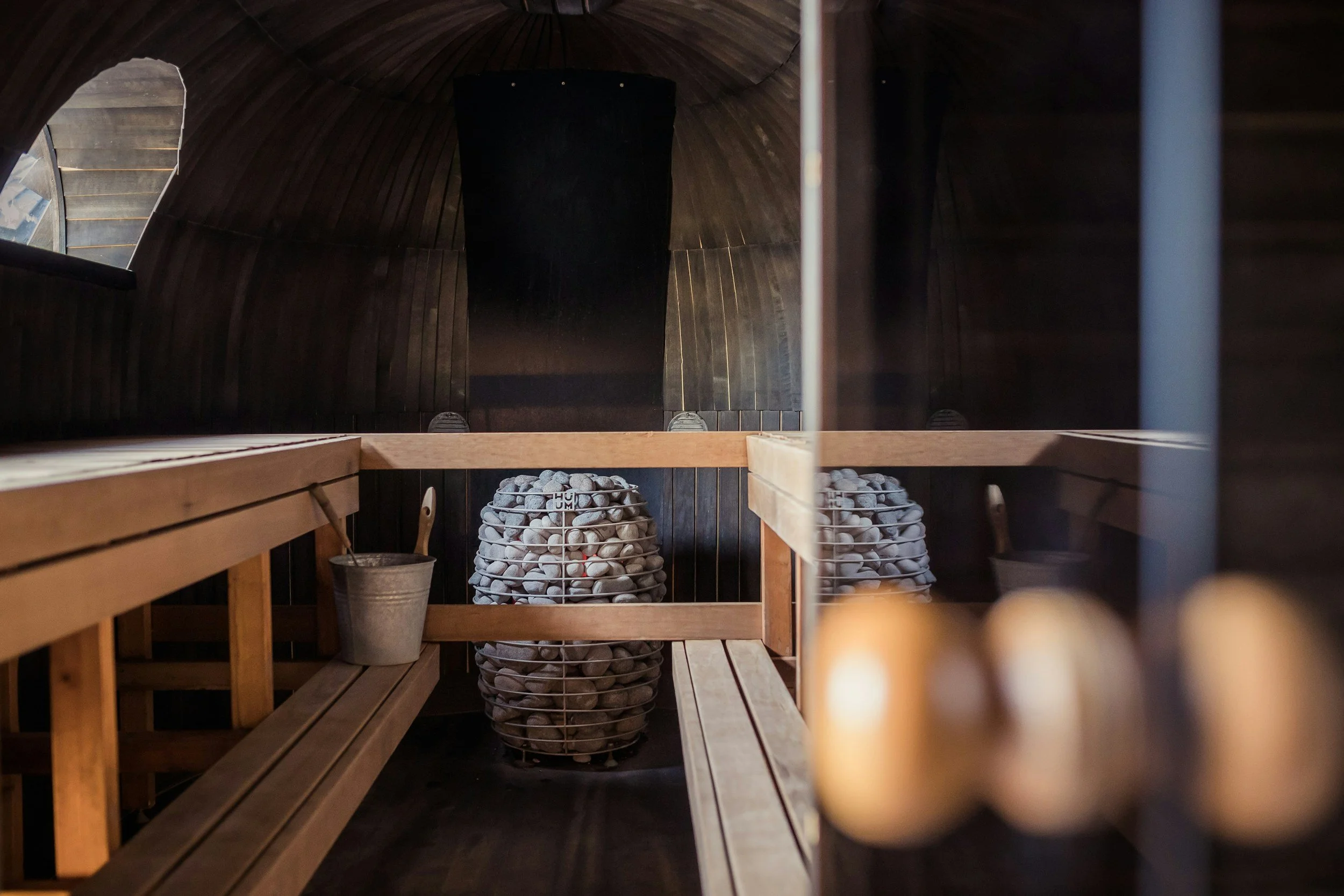 Intérieur d'un sauna en bois avec deux seaux de pierres de sauna, un seau en métal et une petite barre en bois traversant la pièce.
