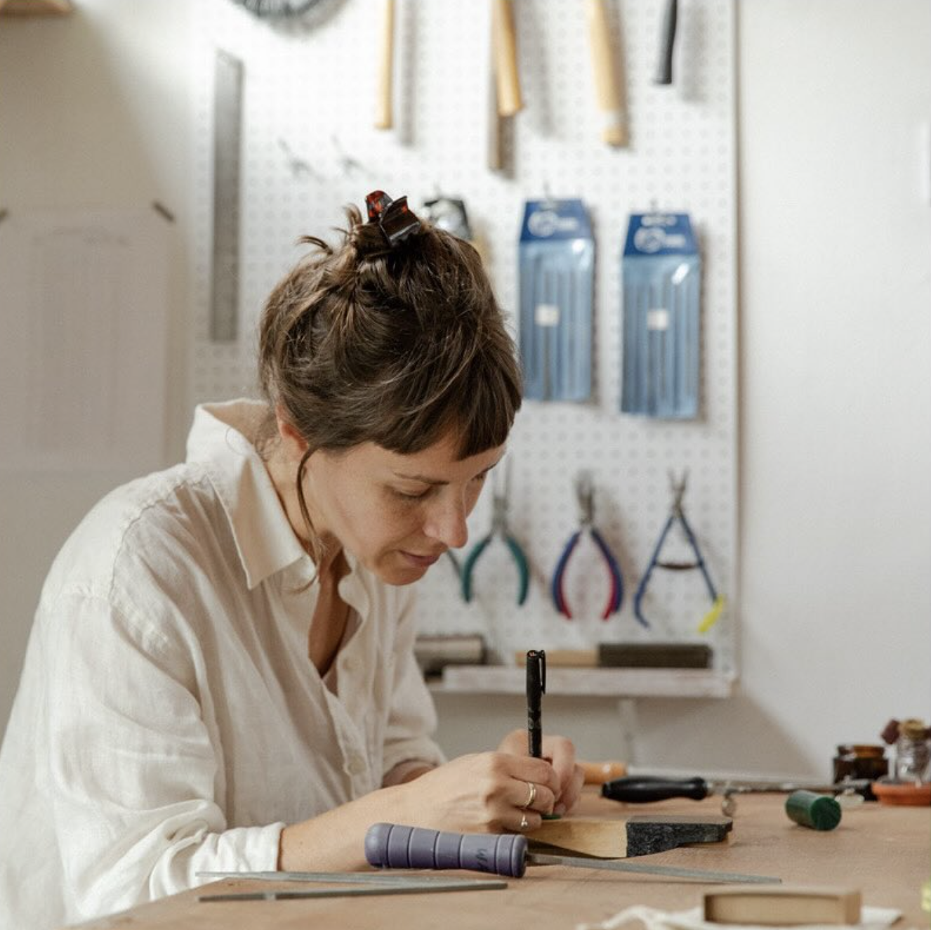 Personne travaillant dans un atelier, utilisant des outils et un stylo. Fond d'étagère avec outils suspendus.