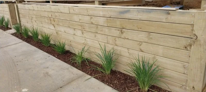 Timber retaining wall for sloping section stabilization