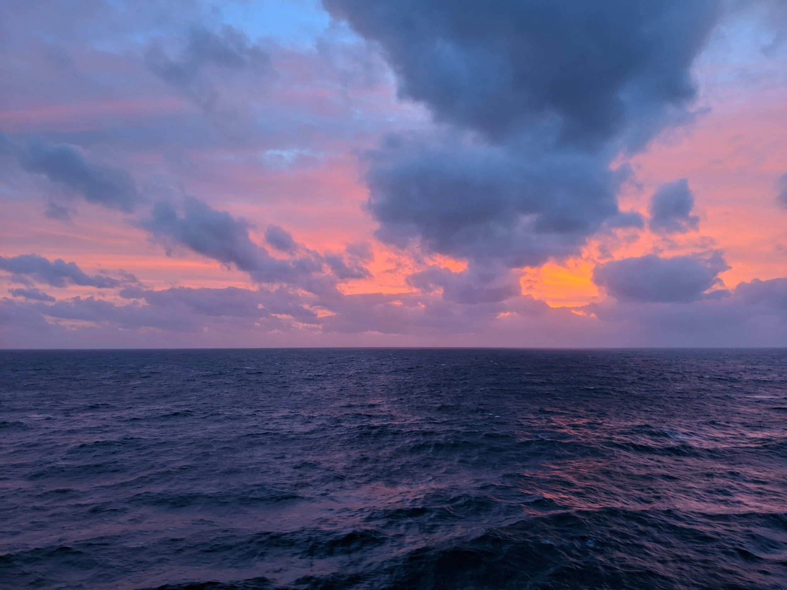 Ocean sunset with vibrant pink, purple, and blue hues in the sky, and dark clouds above the horizon.