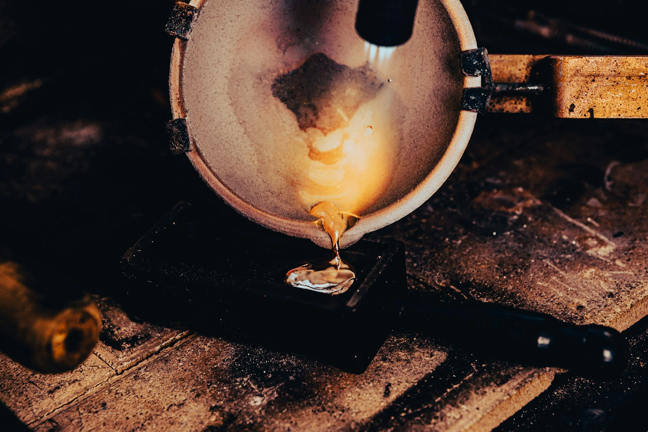 Molten gold pouring from a crucible onto a mold at a foundry or workshop.