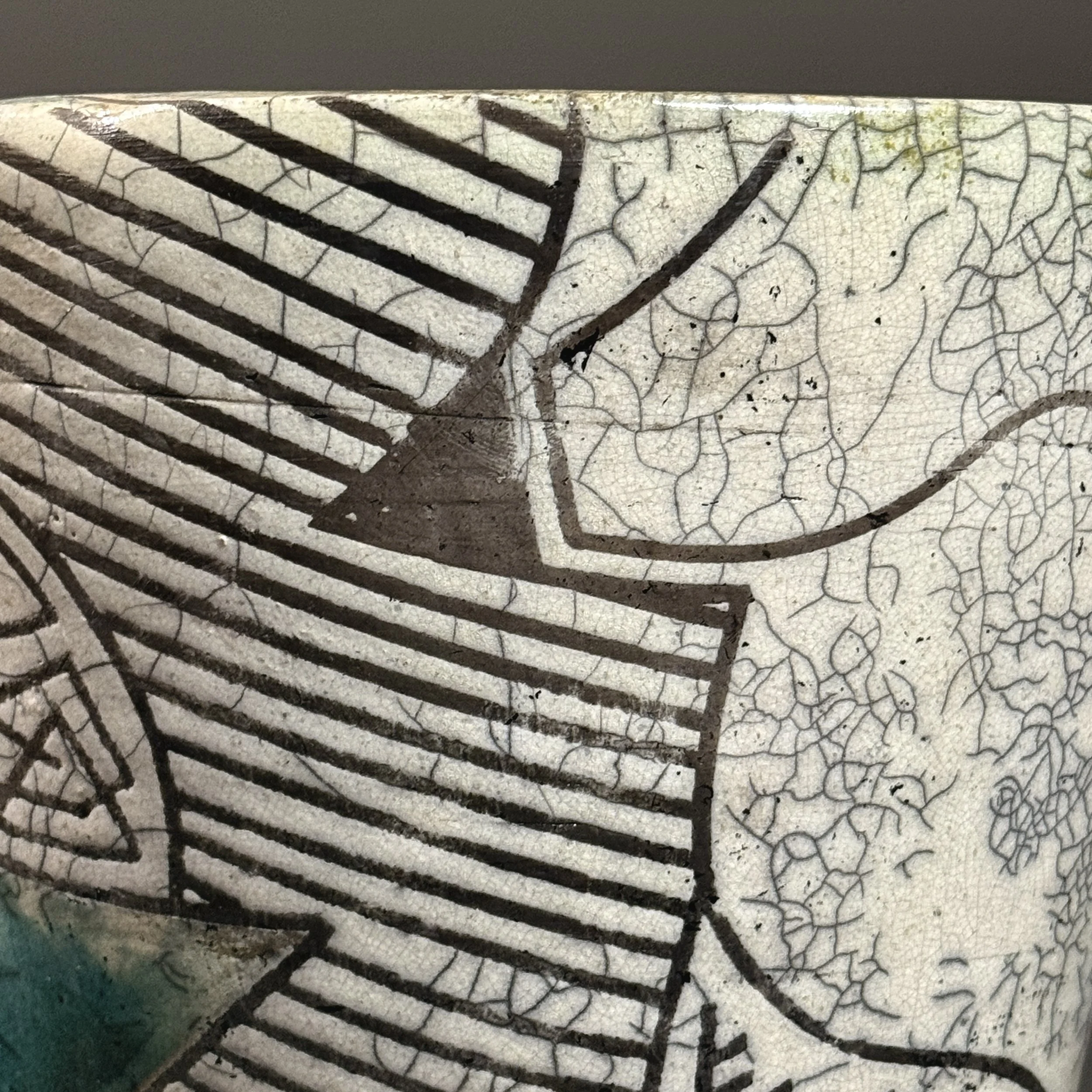 Close-up of blue-green glaze areas on vintage raku vessel with crackle surface and black line detail