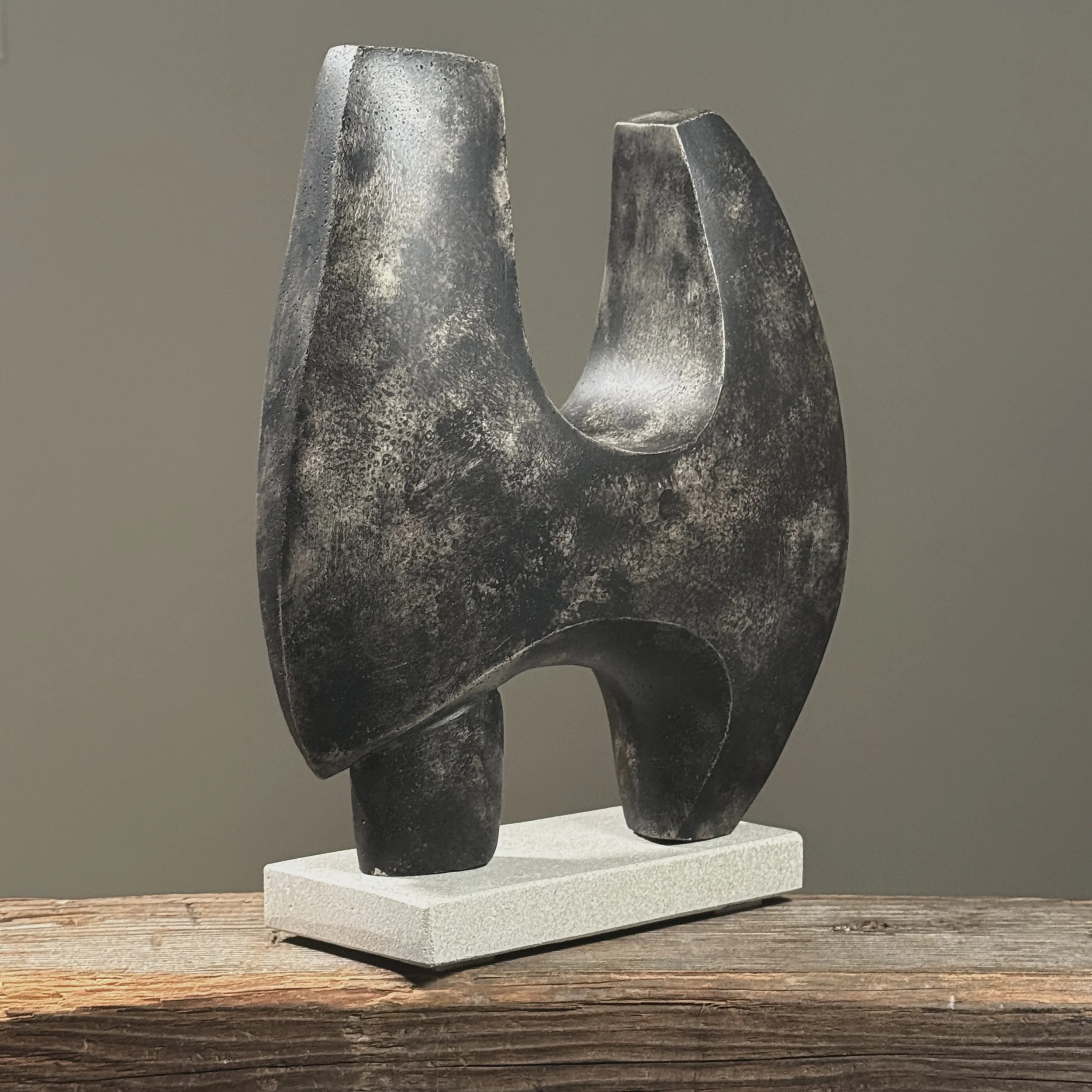 Three-quarter view of an abstract winged sculpture in cement, mounted on lighter colored base