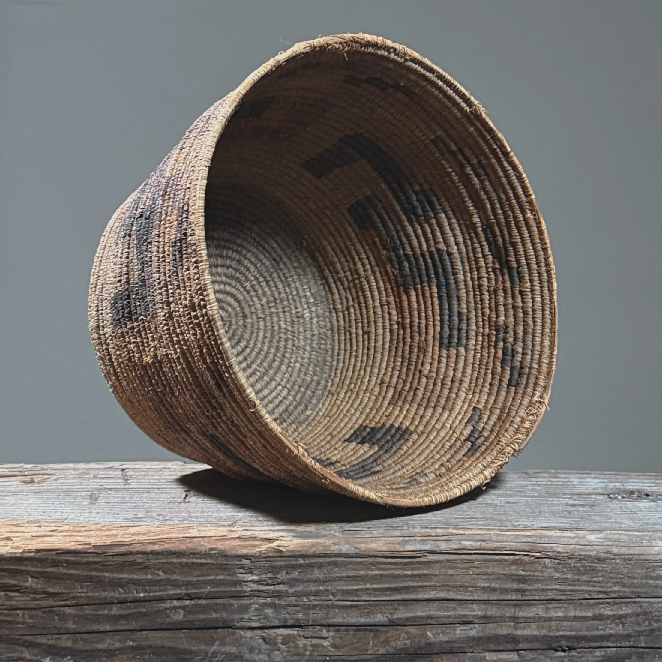 Three-quarter view of a Papago Indian basket woven from yucca and devil's claw with faded design