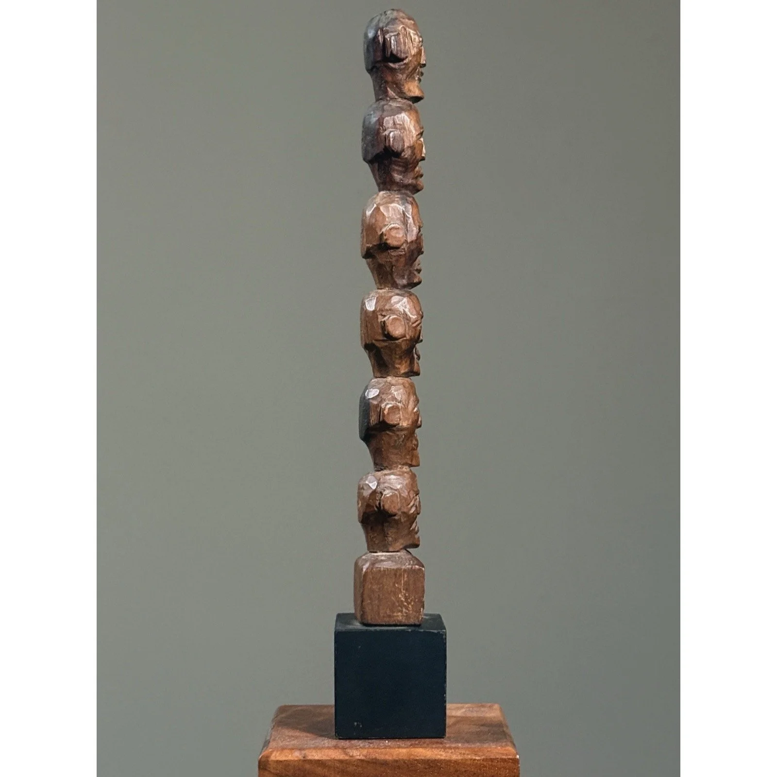 Antique hand-carved wooden head totem on black base, side view.