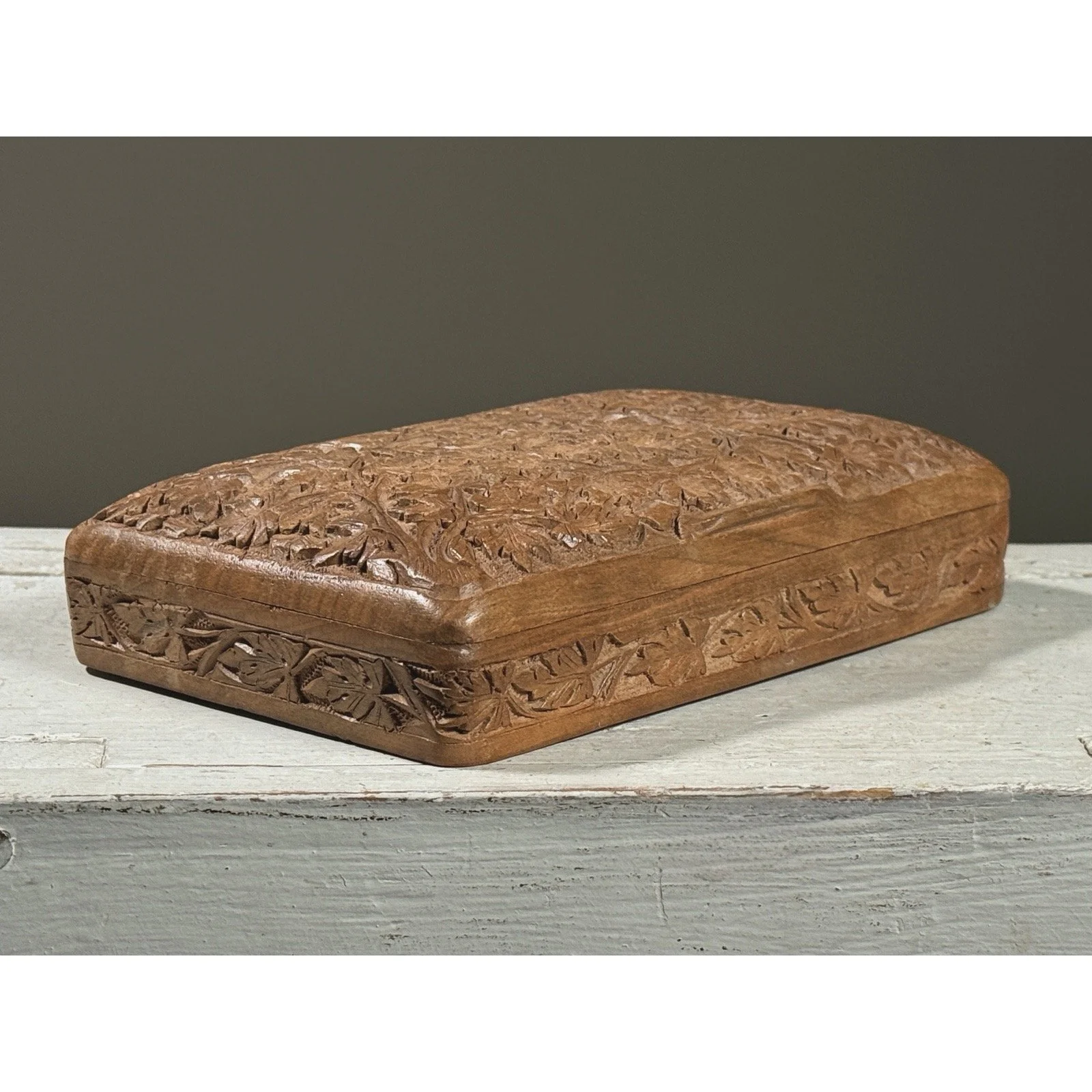 Full frontal view of a vintage hand-carved folk art lidded box with intricate foliage detail on the lid