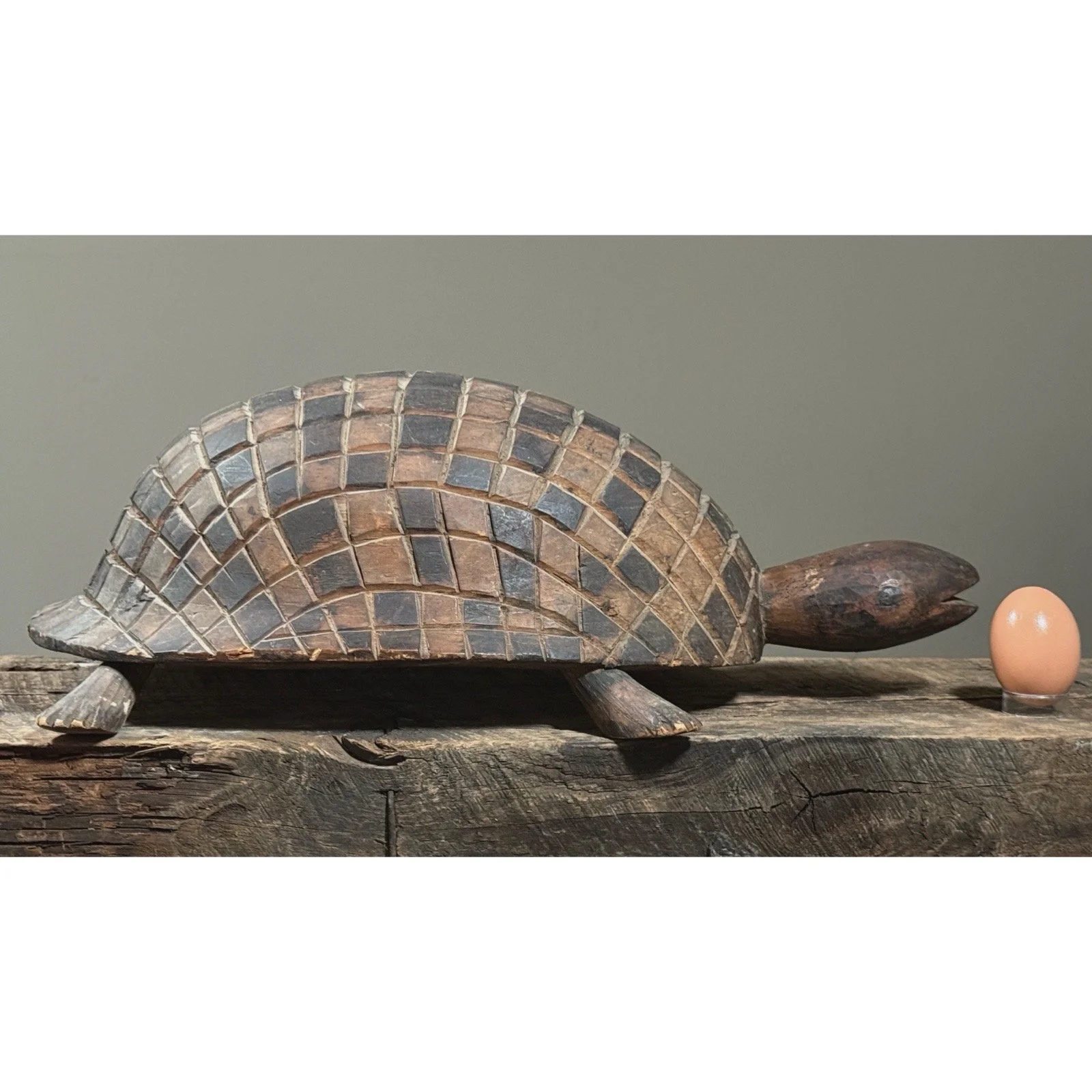 Folk art turtle carving with geometric shell design with egg for size reference.