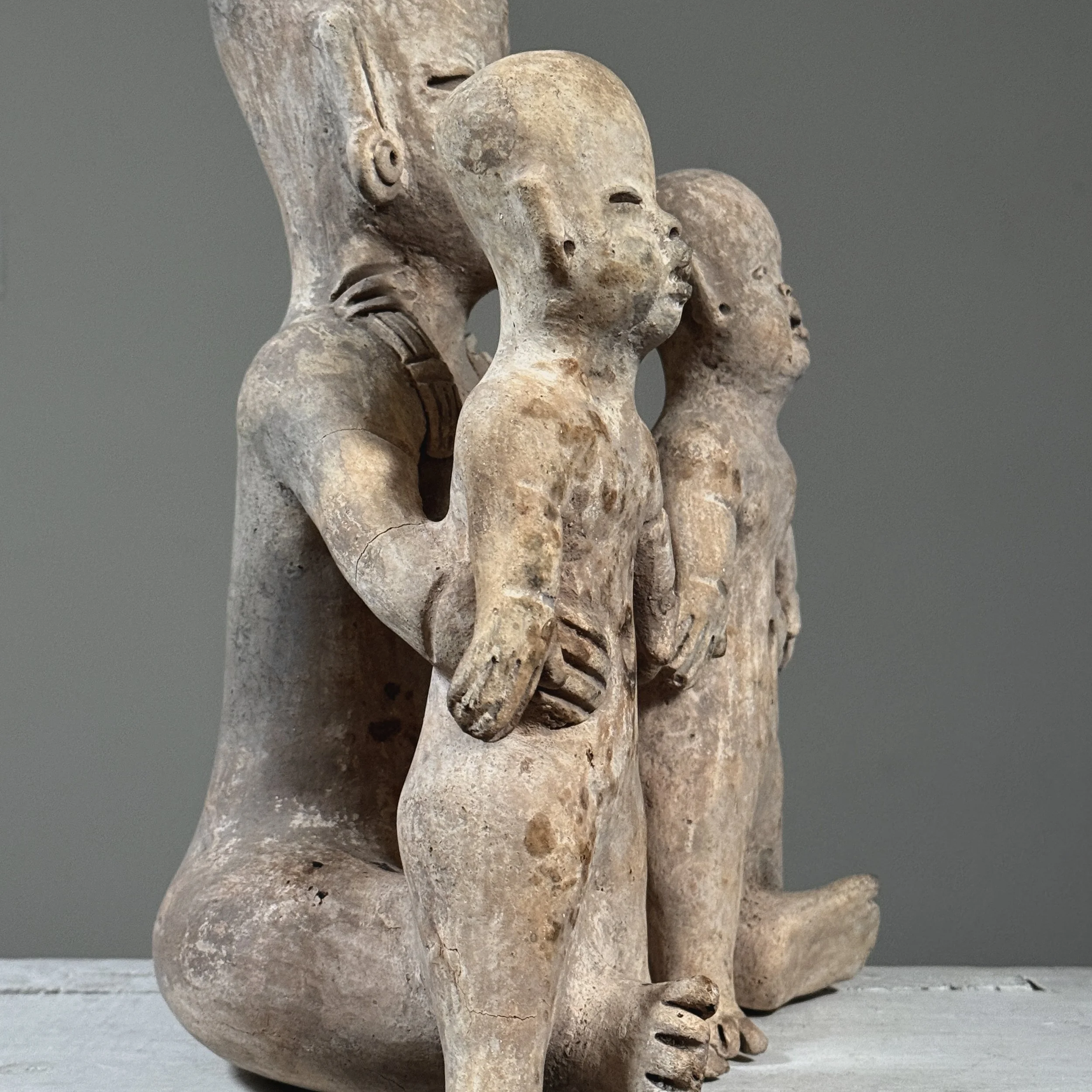 Side view of Antique Olmec style folk art baby sculpture, three terracotta figures, wood fired