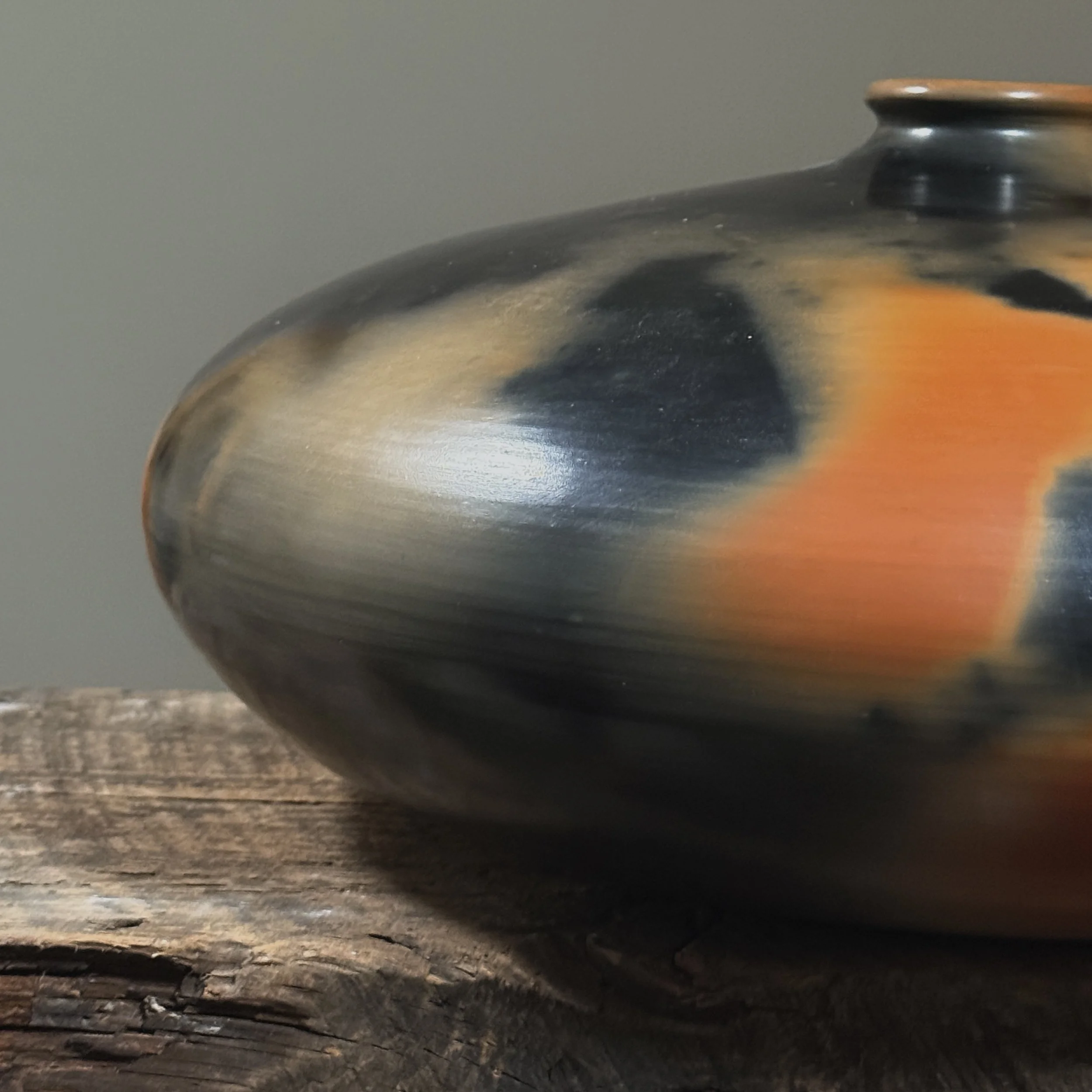 Smoke-fired ceramic pot with bold orange and black coloration.
