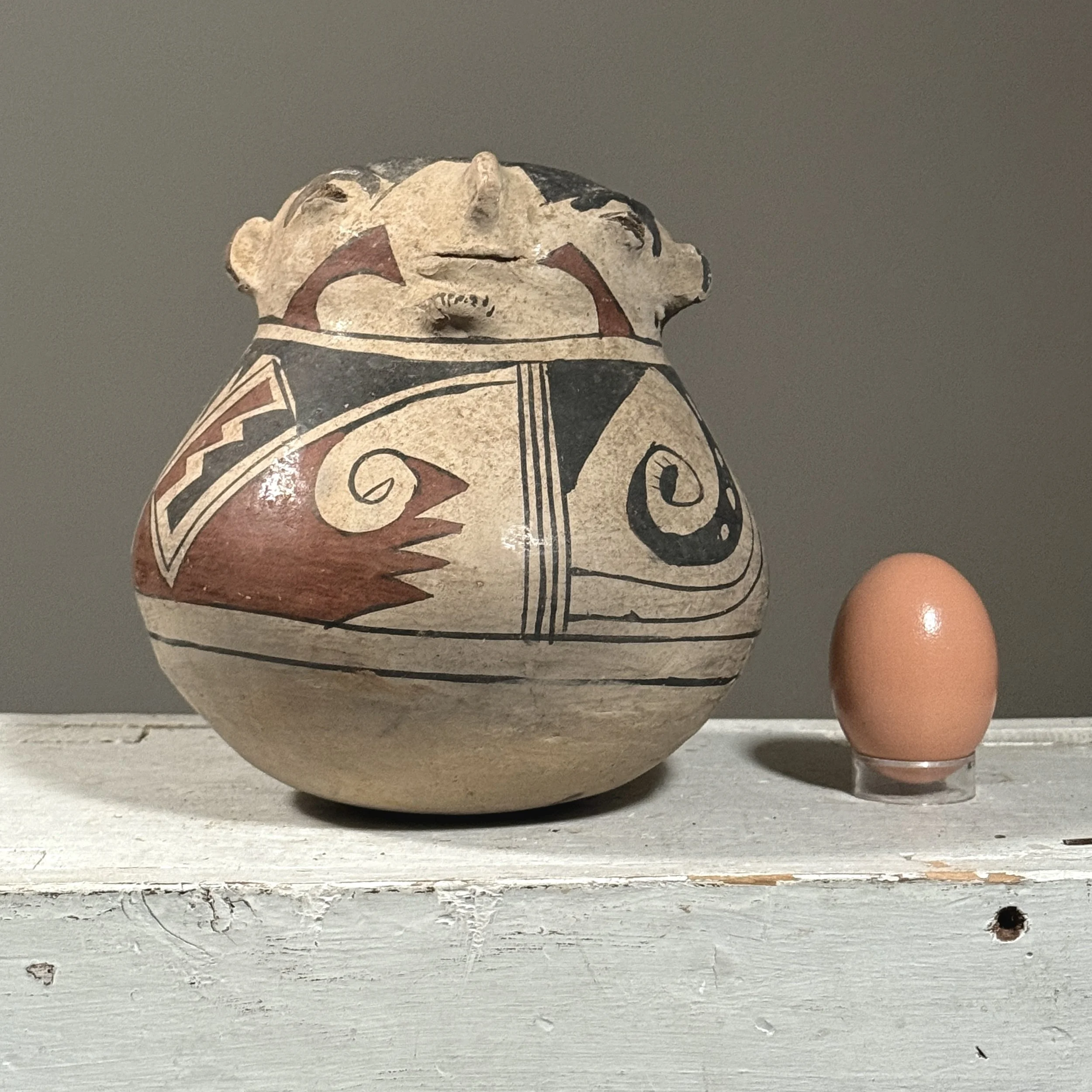 Effigy pot with painted surface and portrait figure with egg for size reference.