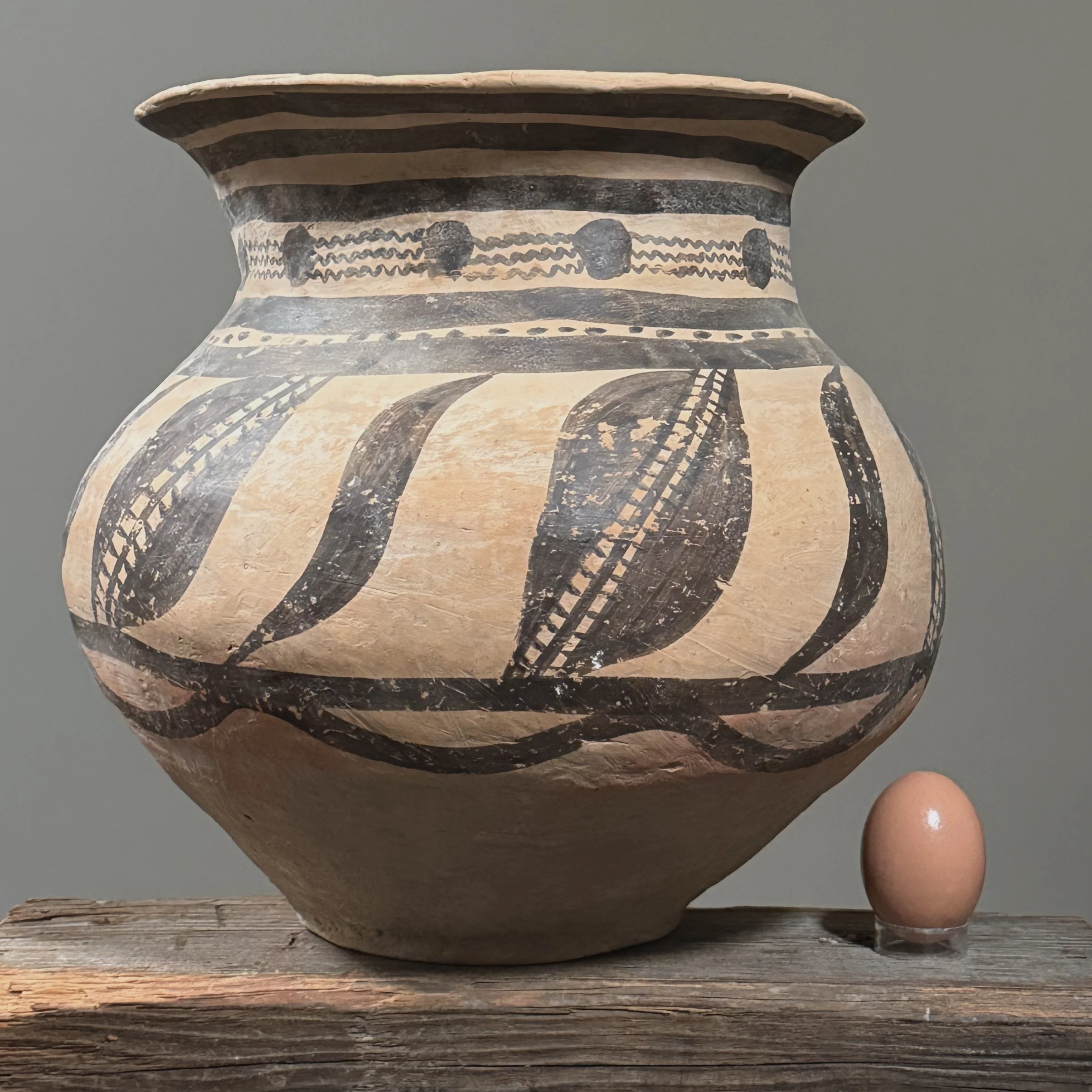 A large pottery jar in the Majiayao style with black geometric patterns with an egg for size reference.