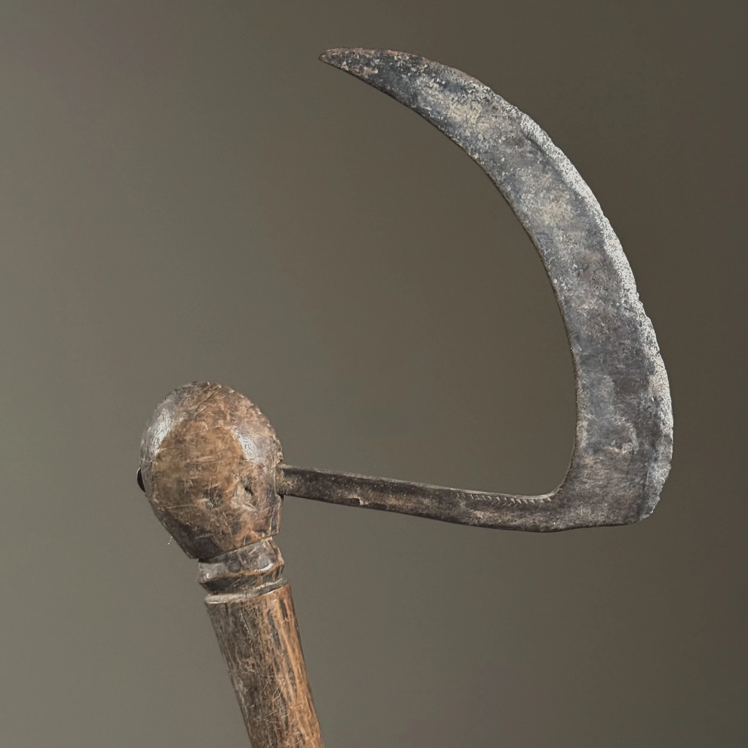 Close-up detail of the carved face where iron blade meets wooden handle