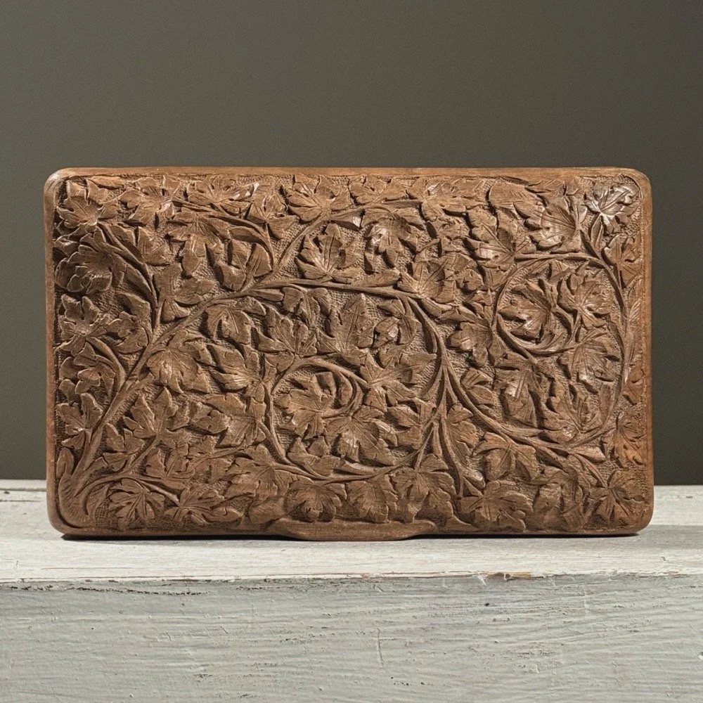 Full frontal view of a vintage hand-carved folk art lidded box with intricate foliage detail on the lid
