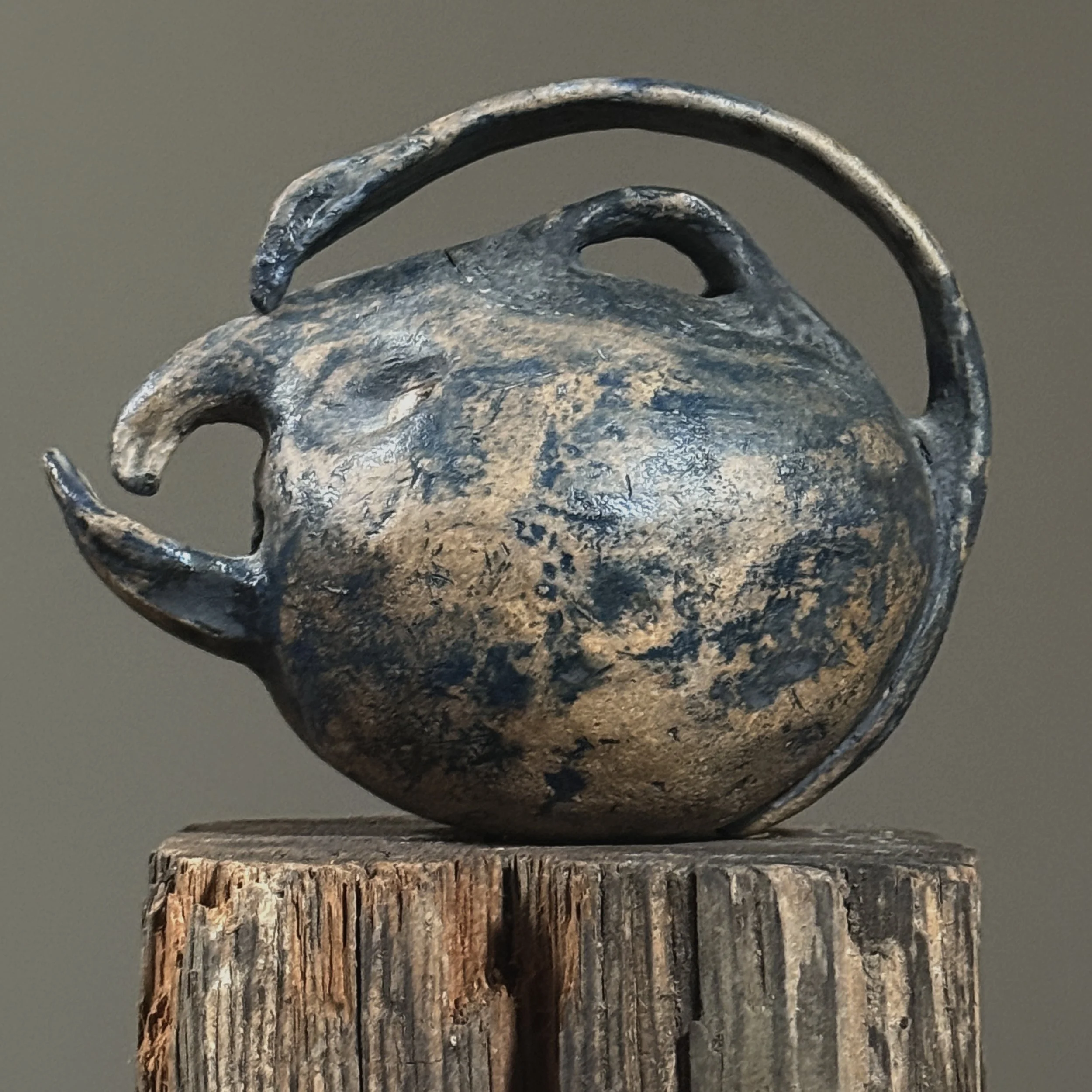 Wood-fired handmade teapot with sculptural facial features, side view.
