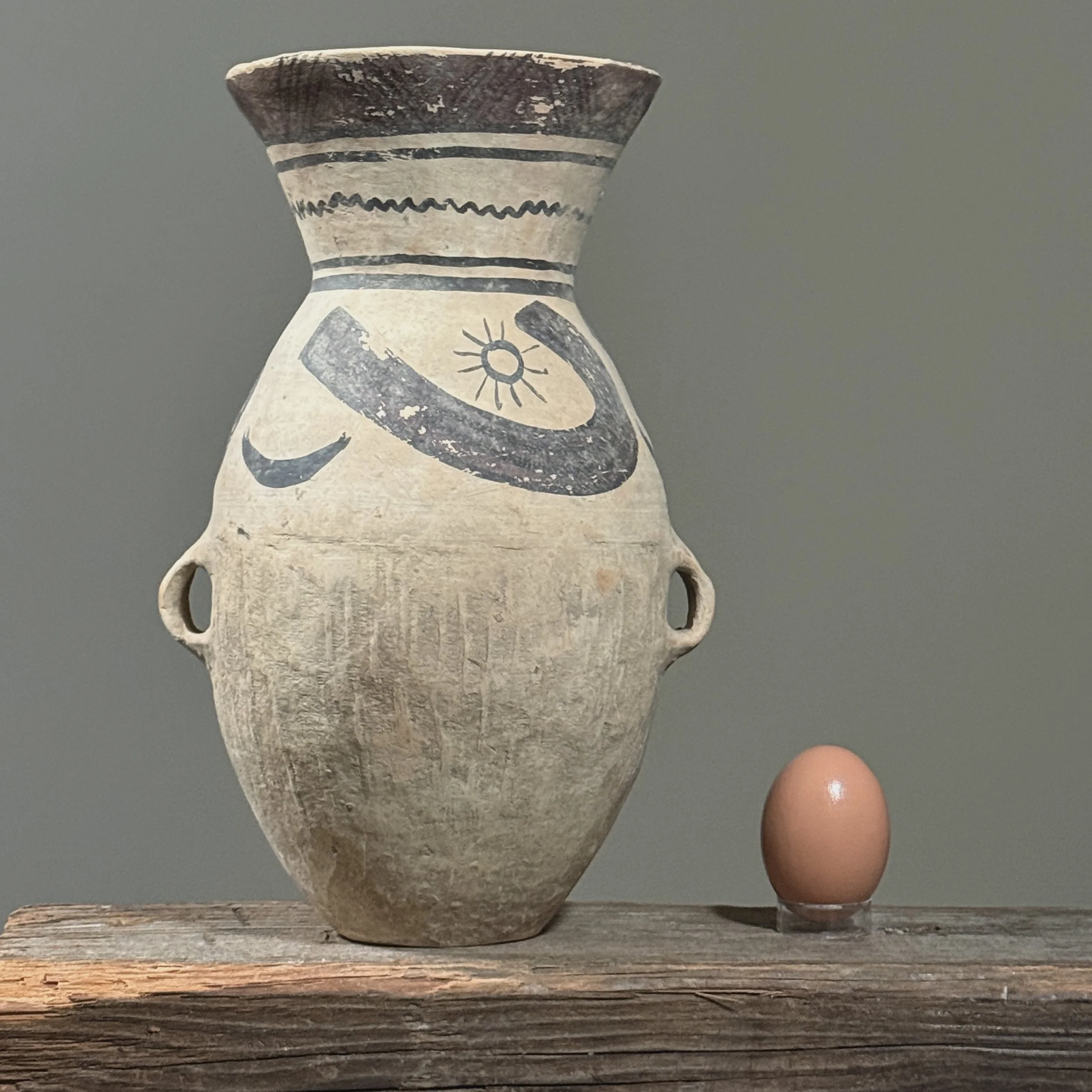 Front view of Ma Jia kiln vessel with polychrome decoration with egg for size reference.