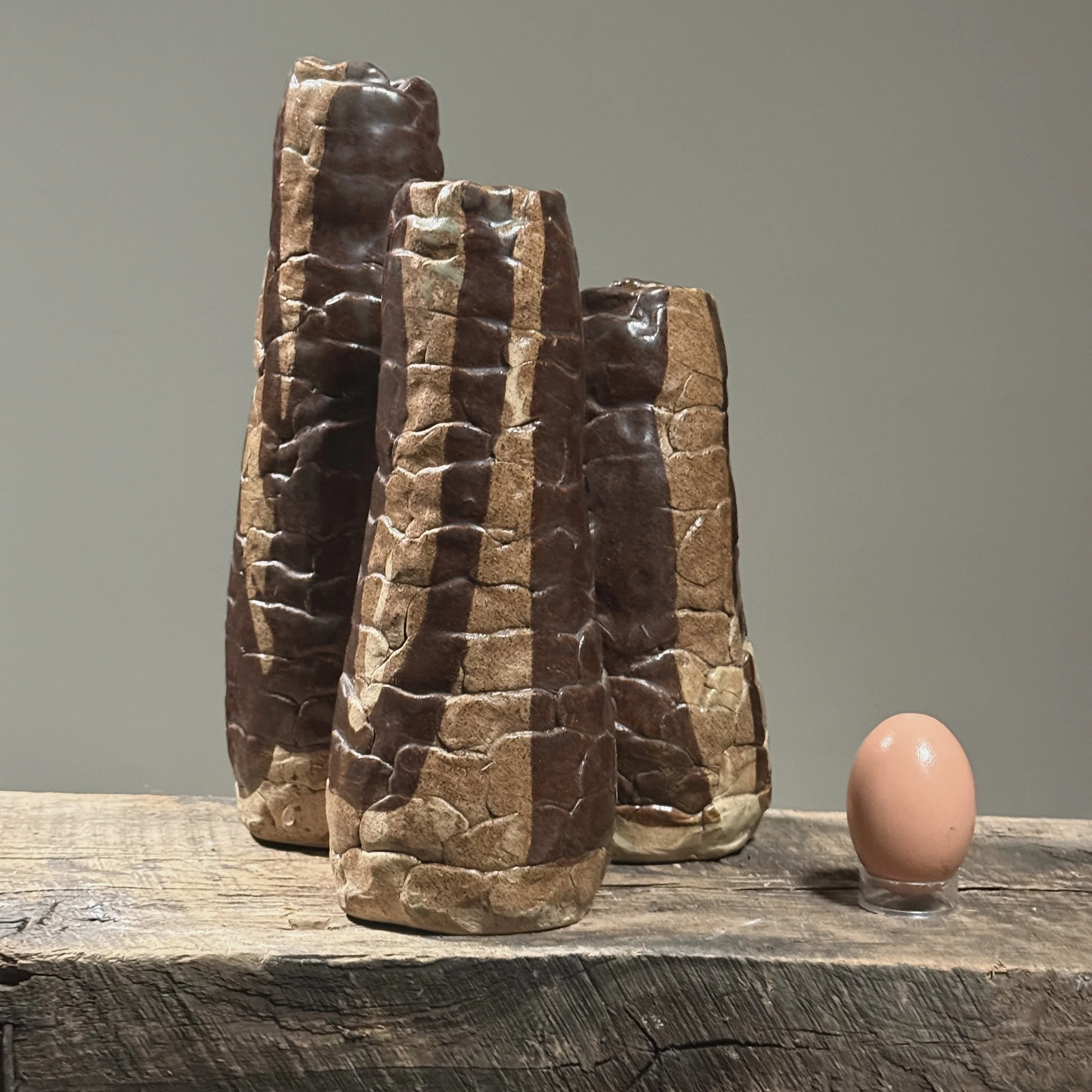 Full frontal view of a vintage Brutalist hand-built ceramic vessel with three connected cylindrical forms With egg for size reference.