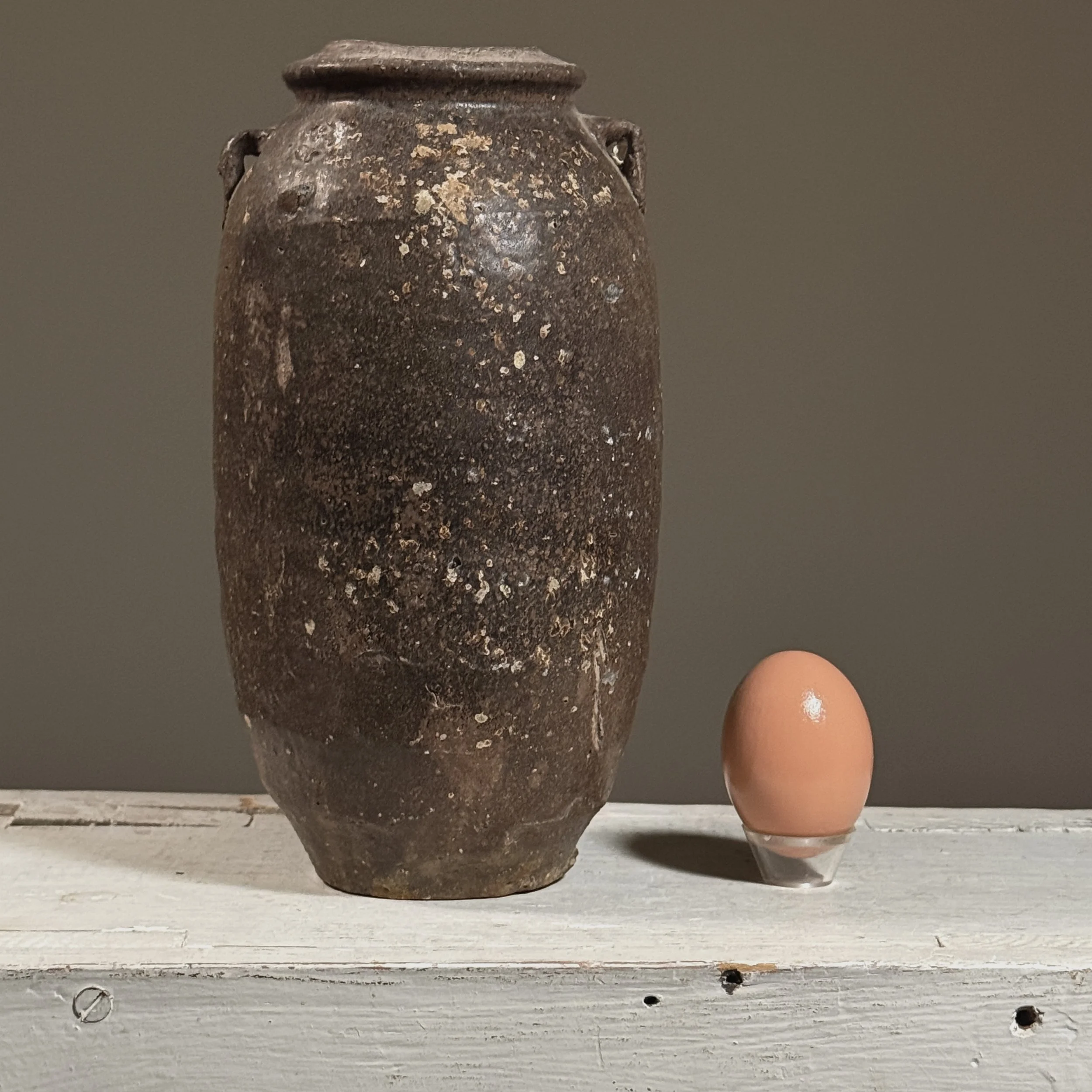 Full view of a 17th-century Vietnamese brown-glazed stoneware jar with lug handles with egg for size reference.