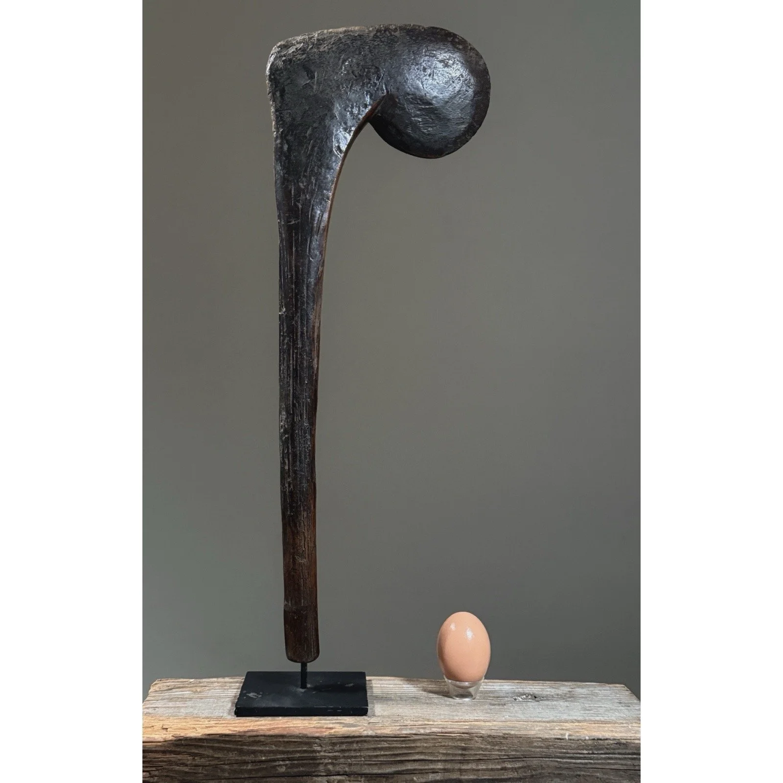 A hand-carved wooden ceremonial scepter from Burkina Faso, Bobo-style, on a black metal stand with egg for size reference.