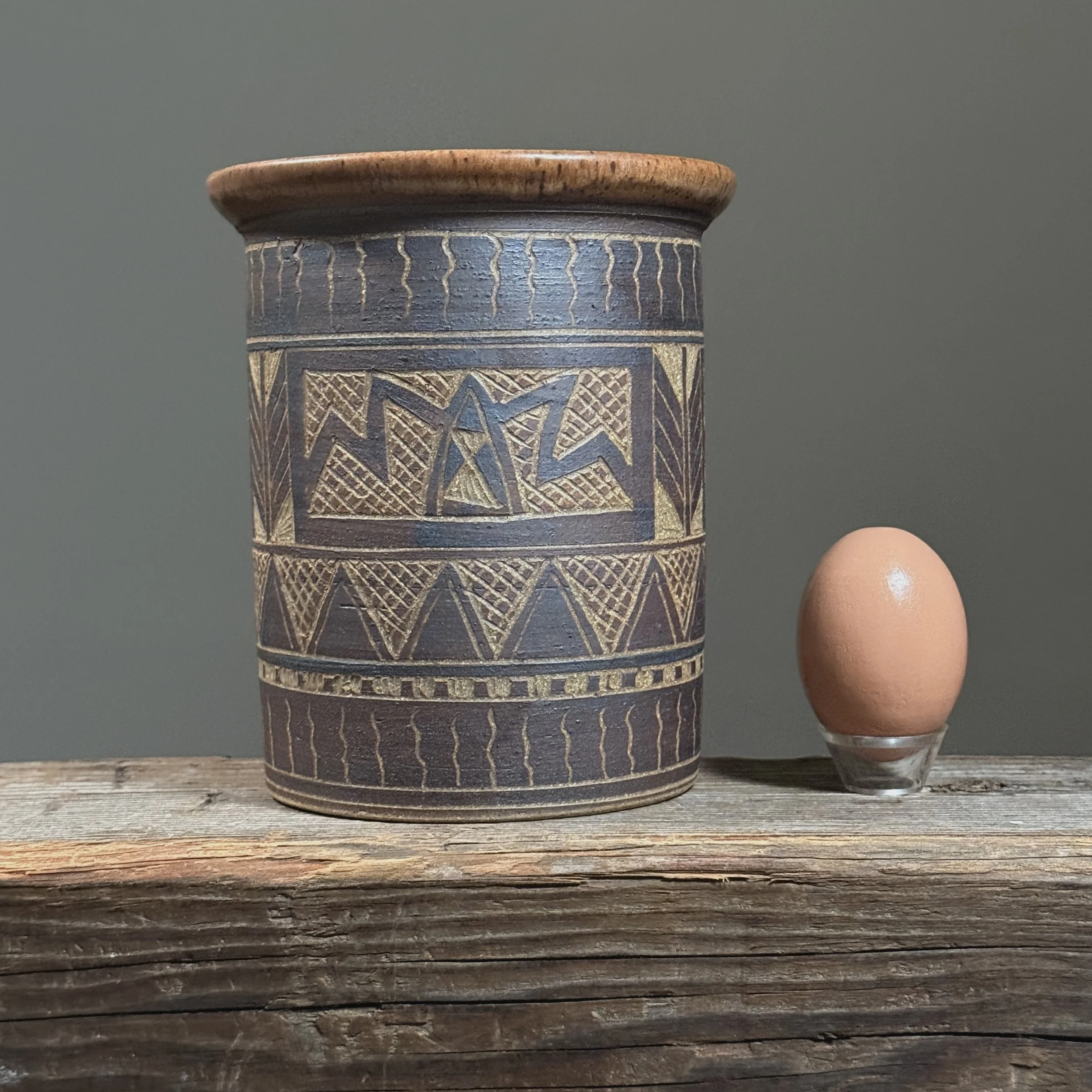 Full frontal view of a vintage sgraffito ceramic vase with geometric folk art design with an egg for size reference.