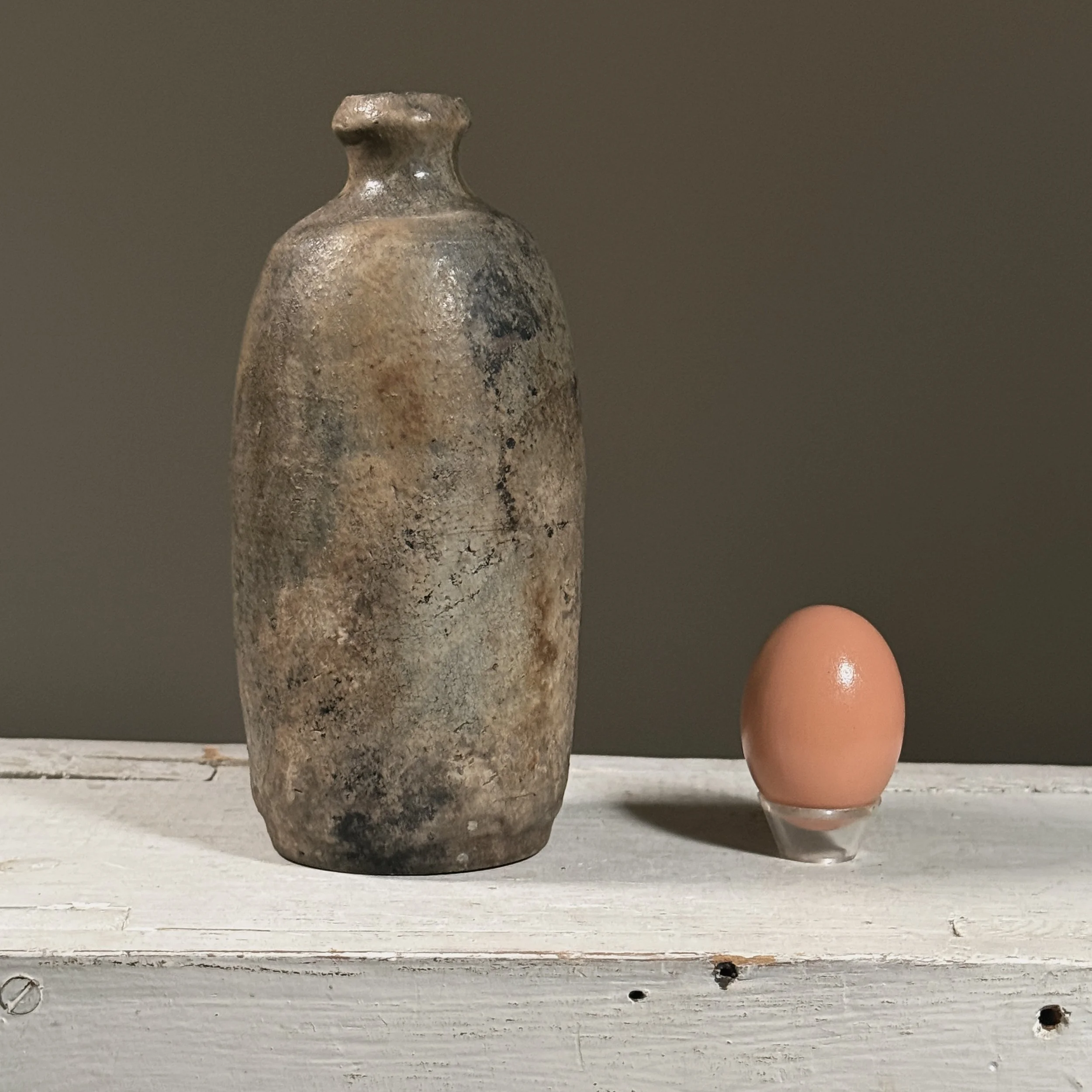 Front view of a Japanese ash-glazed stoneware tokkuri (sake bottle) with egg for size reference.