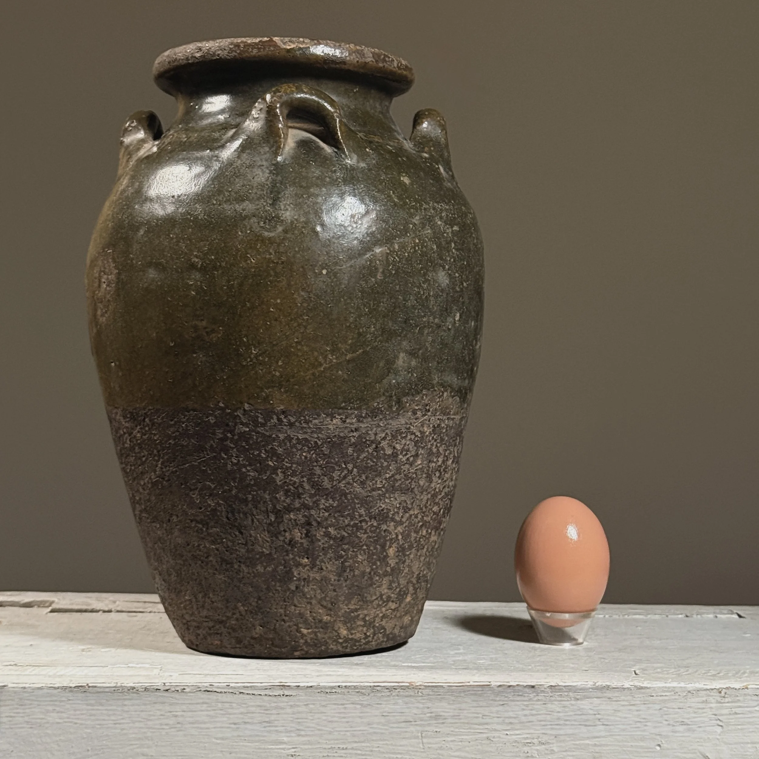 Front view of a Thai Sawankhalok glazed jar with four loop handles with egg for size reference.