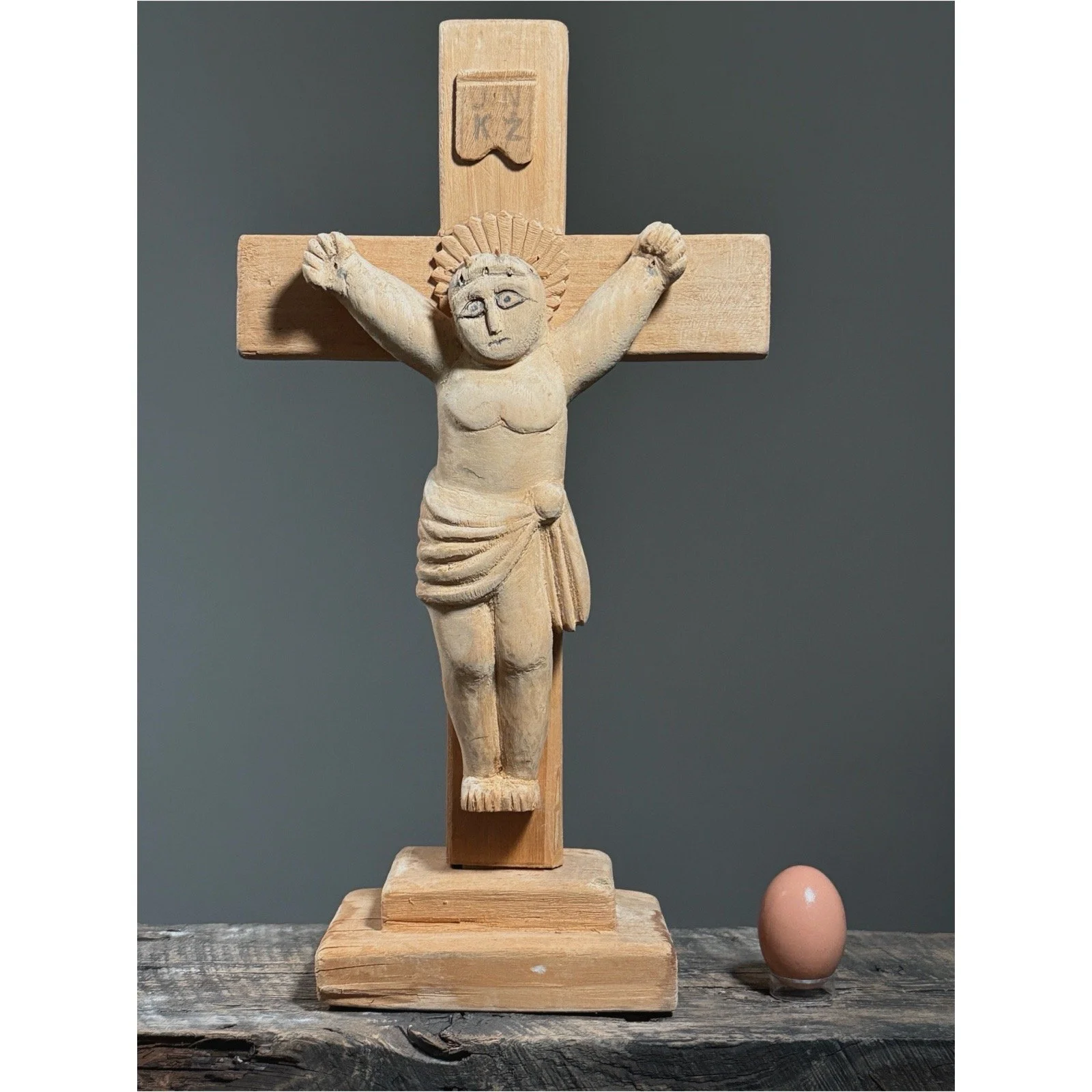 Vintage European hand-carved wooden crucifix sculpture with egg for size reference.
