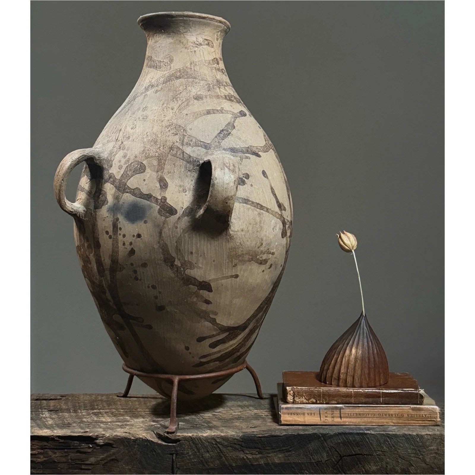 Vintage Tonaltepec amphora-style handled clay vessel on custom metal stand, vignette with books and vase.