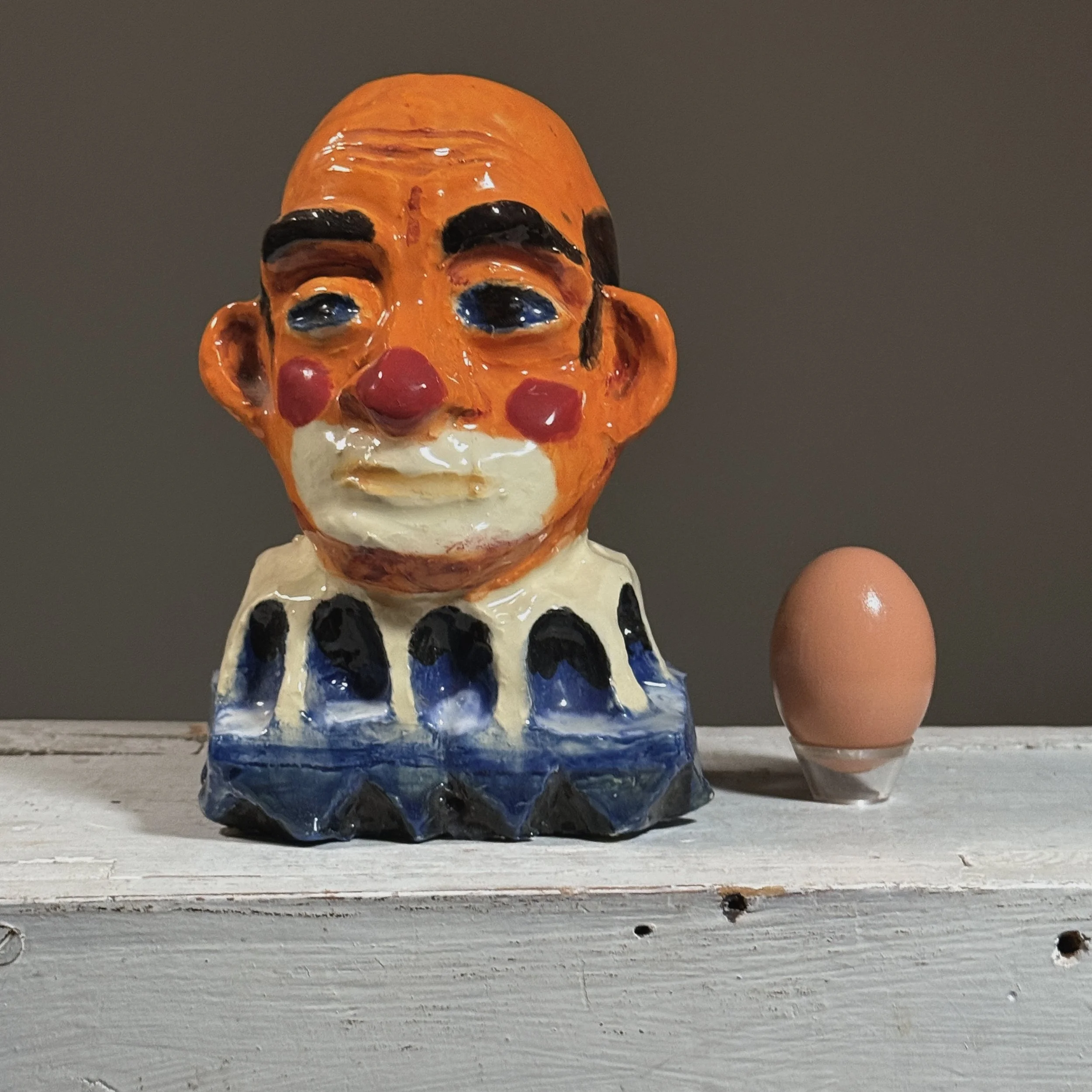 Full frontal view of a vintage expressionist polychrome plaster clown bust by Jack Gerber with egg for size reference
