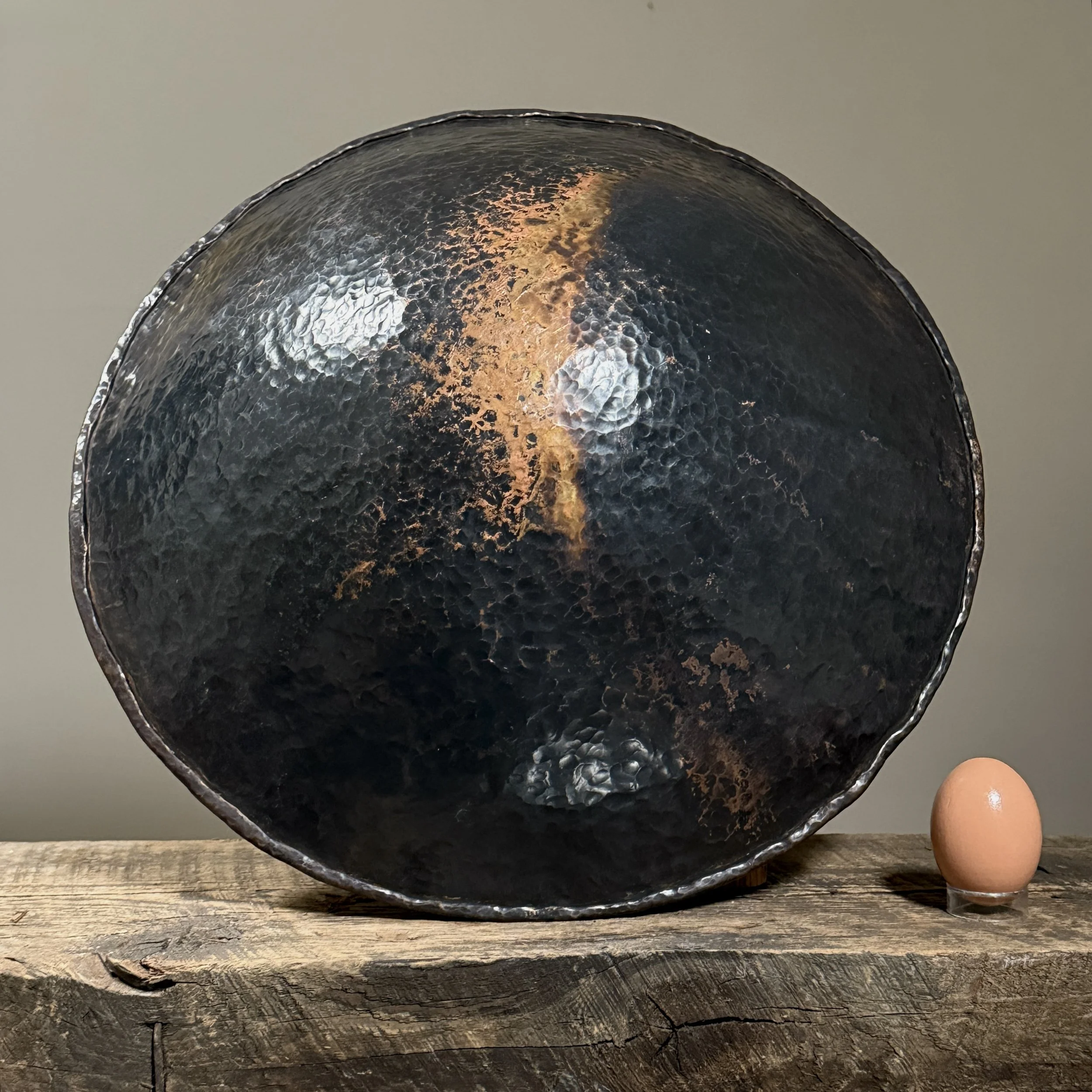 Hand-hammered copper bowl showing textured patina and organic form with egg for size reference.