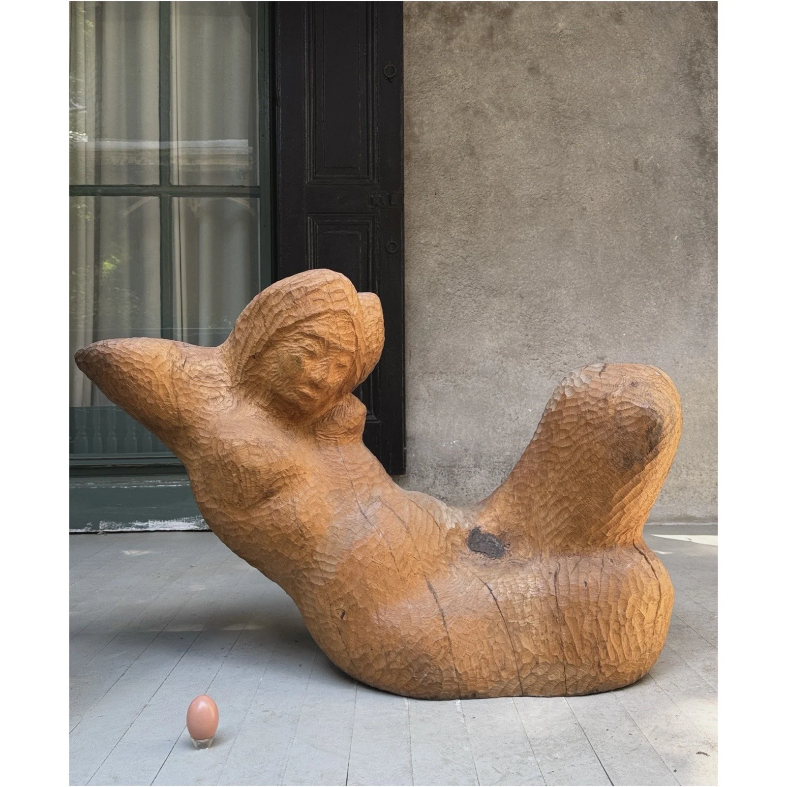 Full frontal view of a vintage monumental modernist wood sculpture of a reclining woman with egg for size reference